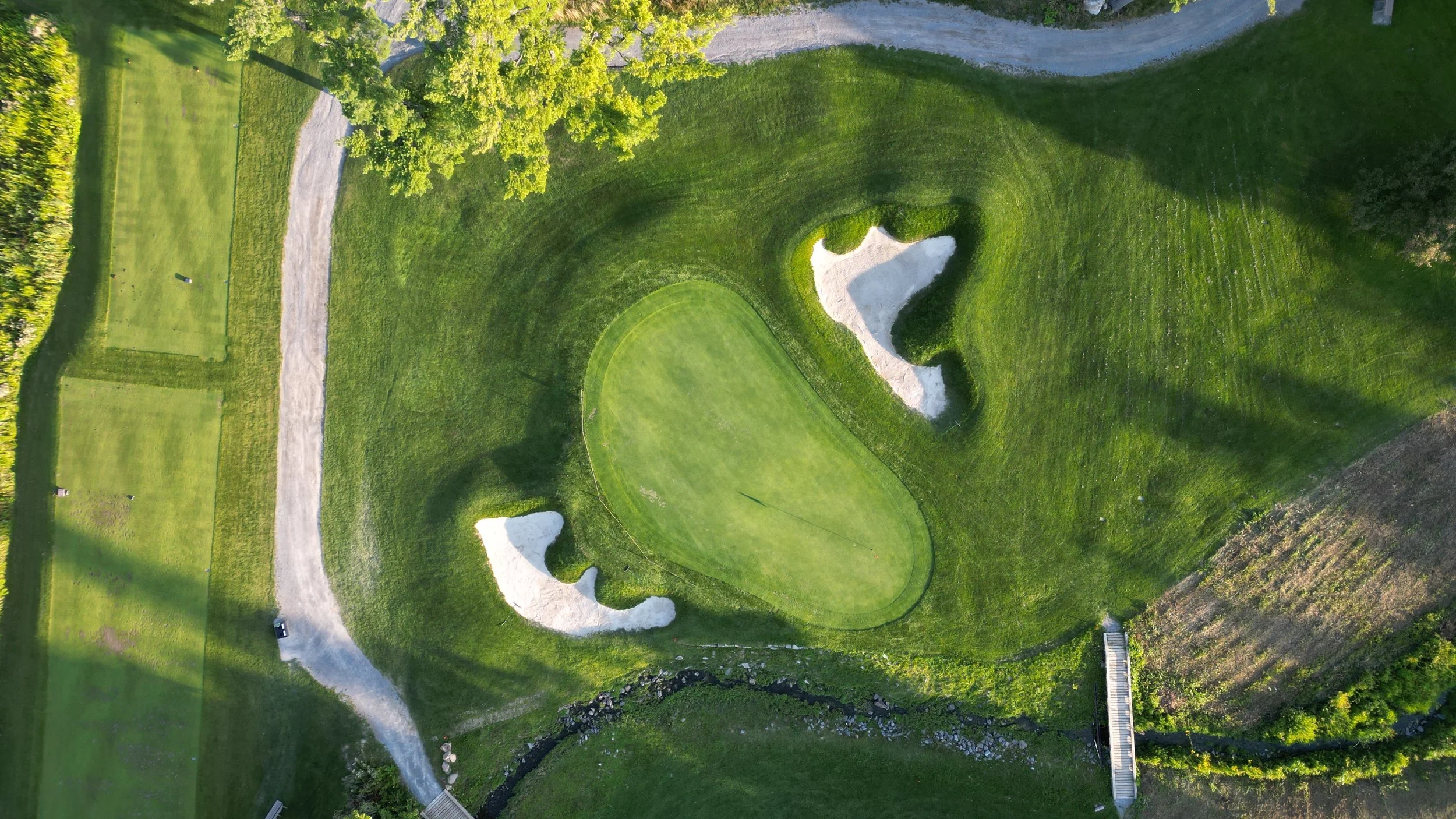 A golf course with a green and sand bunkers surrounded by trees.