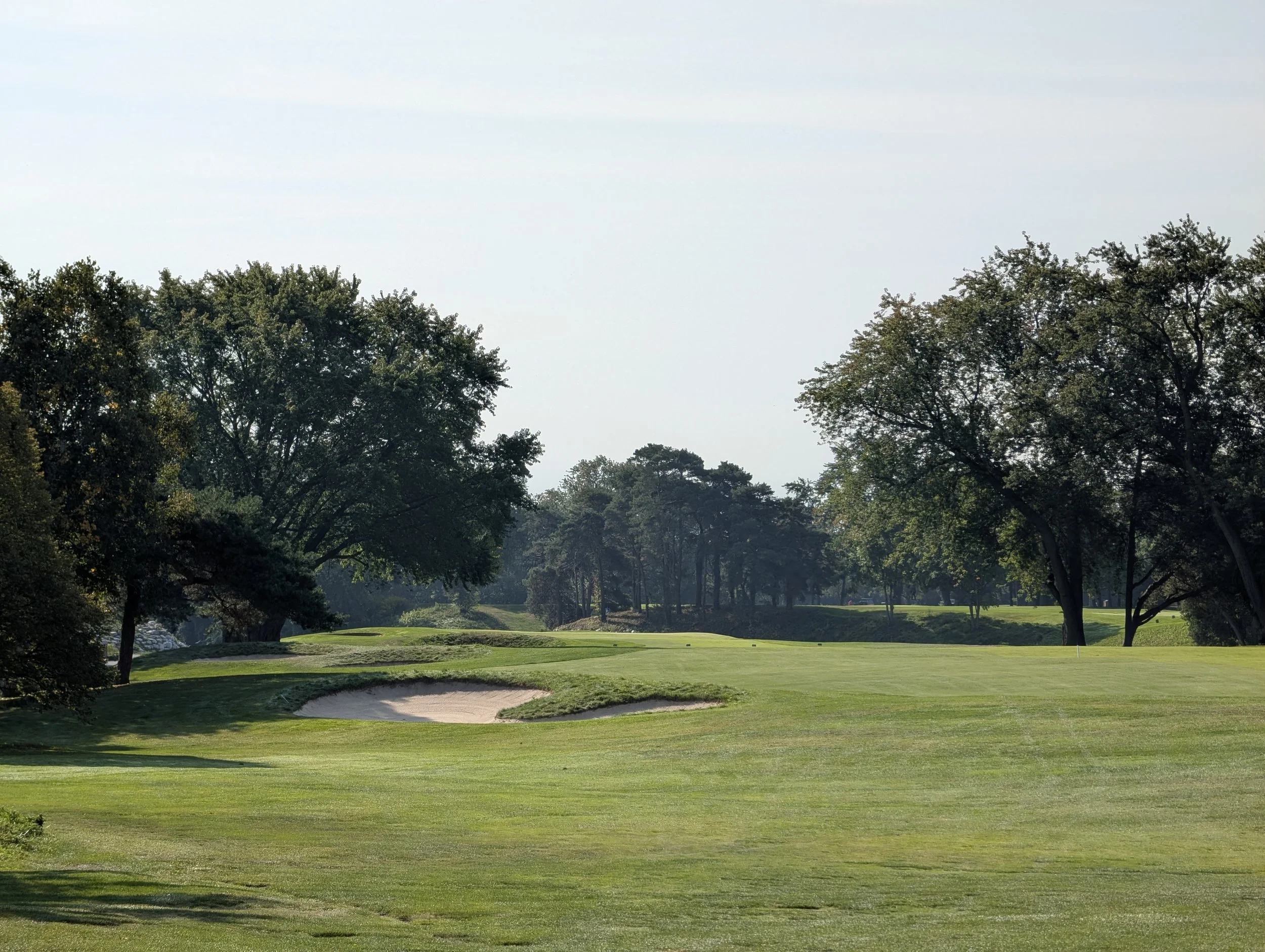 A golf course with green fairways, sand traps, and trees under a clear sky.