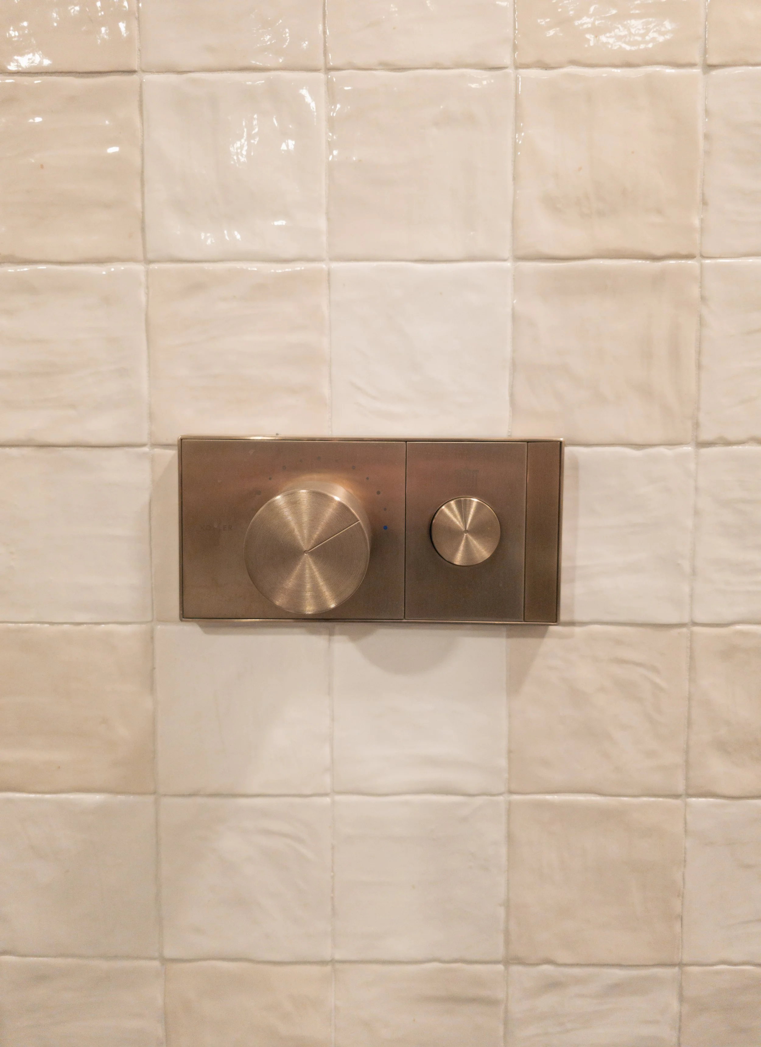 Two metallic flush buttons on a beige tiled wall, one large and one small, for a toilet.