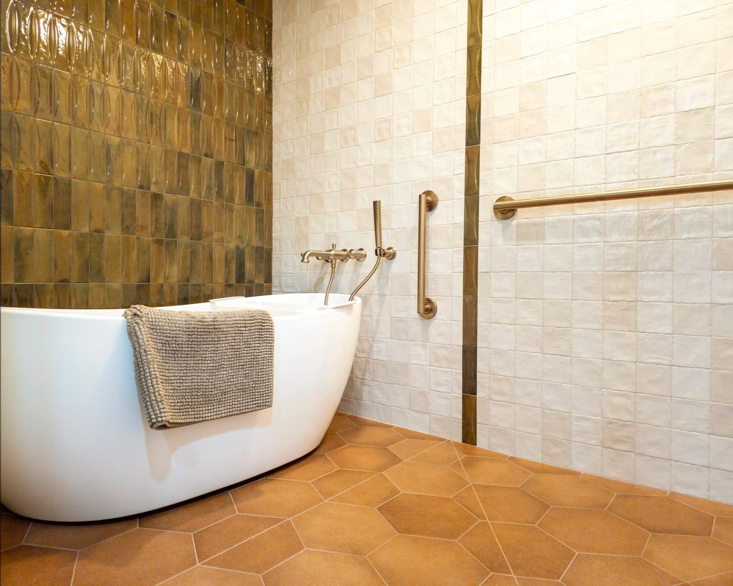 Modern bathroom with a freestanding bathtub, zellige wall tiles, and a terracotta hexagonal tile floor.