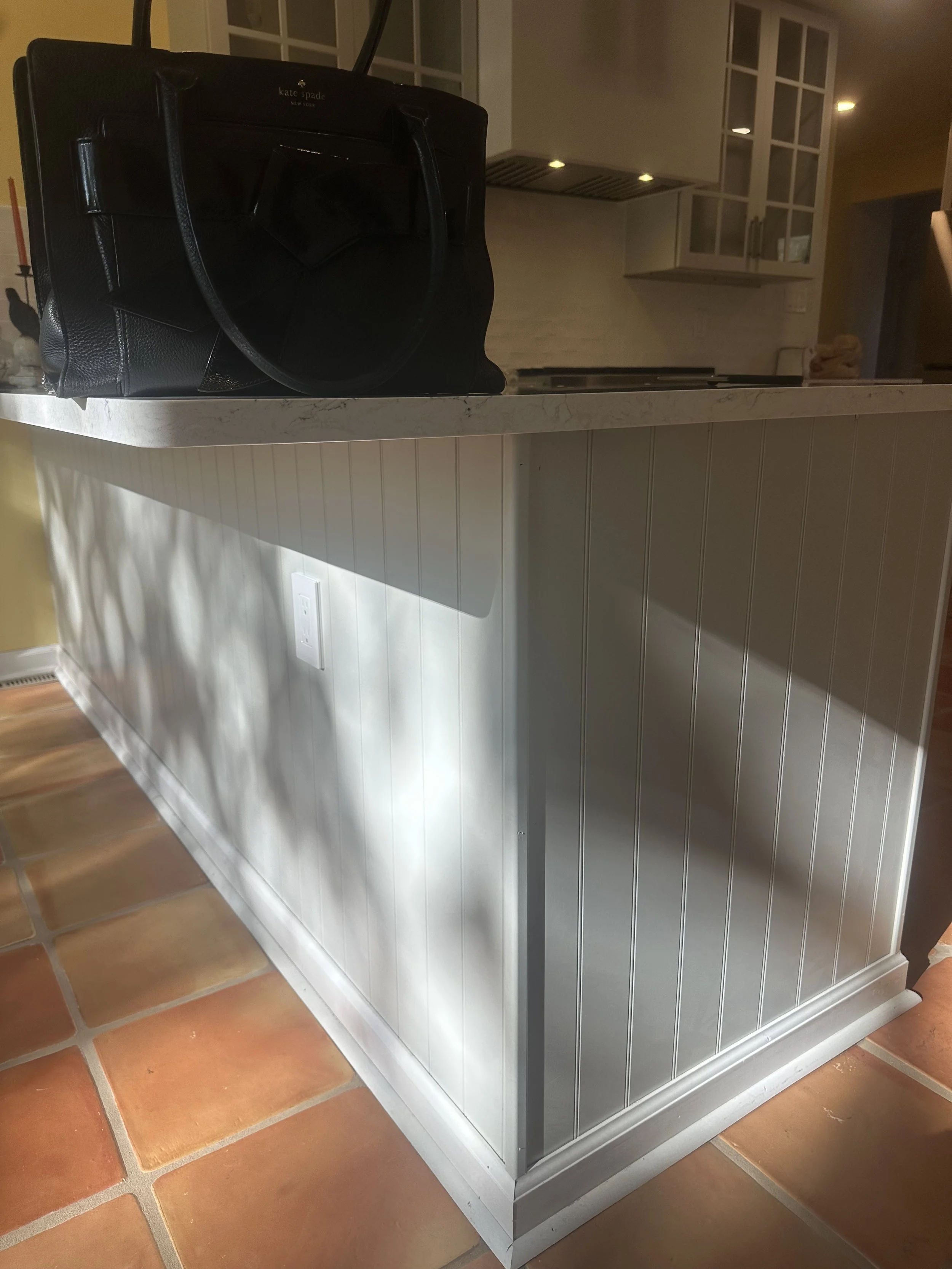 Kitchen island with a dark handbag on the marble countertop, fallow tile flooring, and white kitchen cabinets and walls.