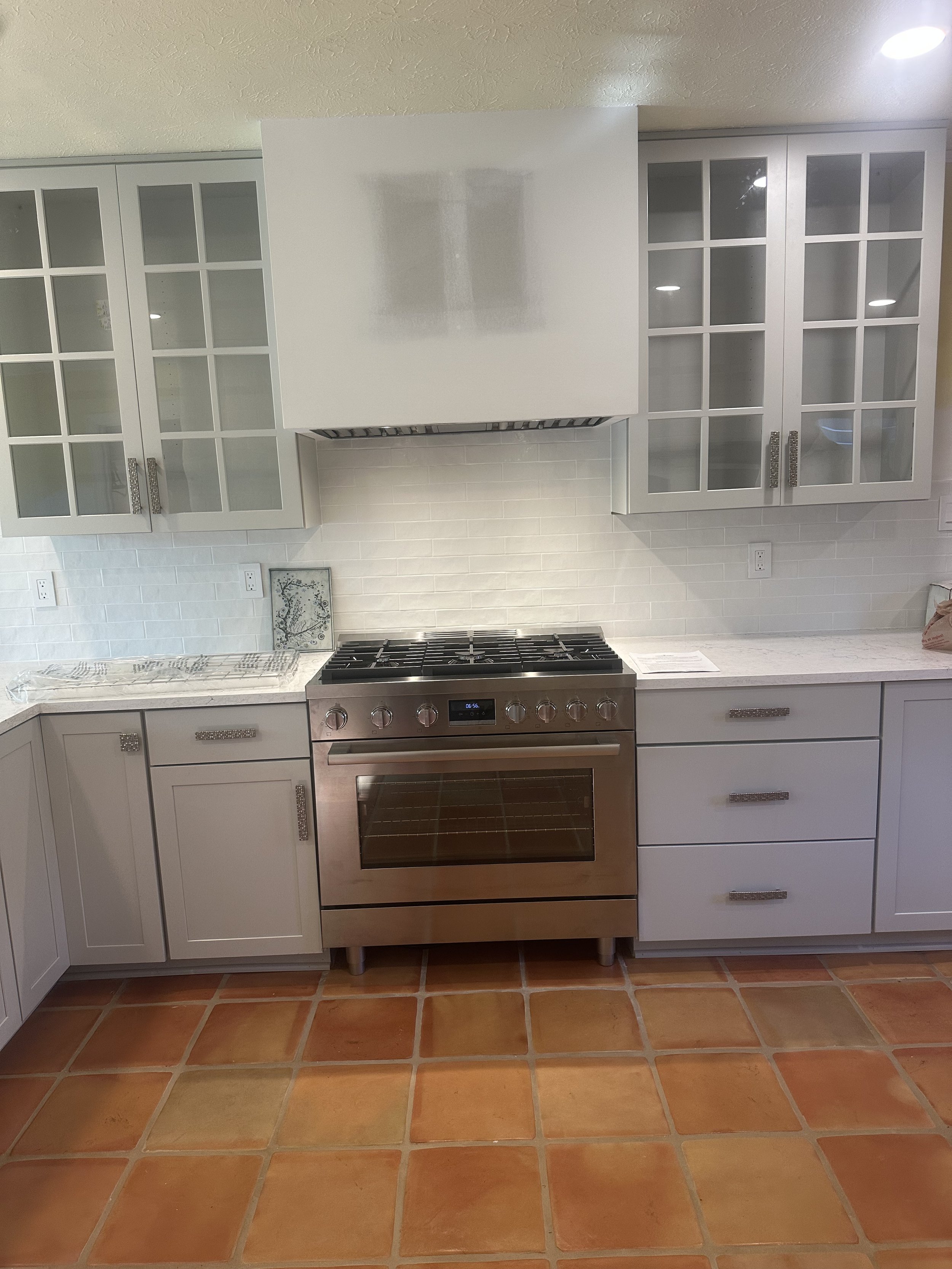 Kitchen with white cabinets, stainless steel oven, and terracotta tile flooring.
