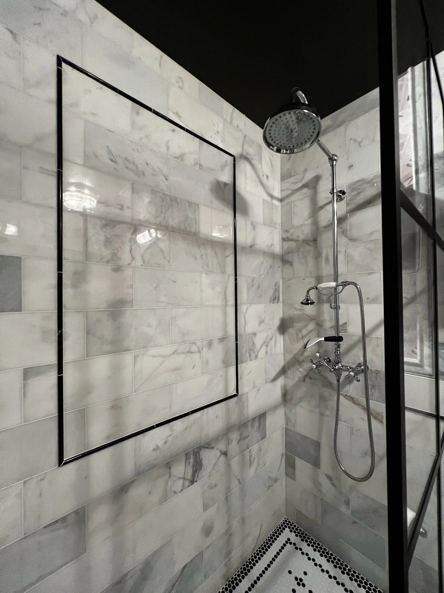 A modern shower with marble tiles, a rain shower head, and a black metal frame design.