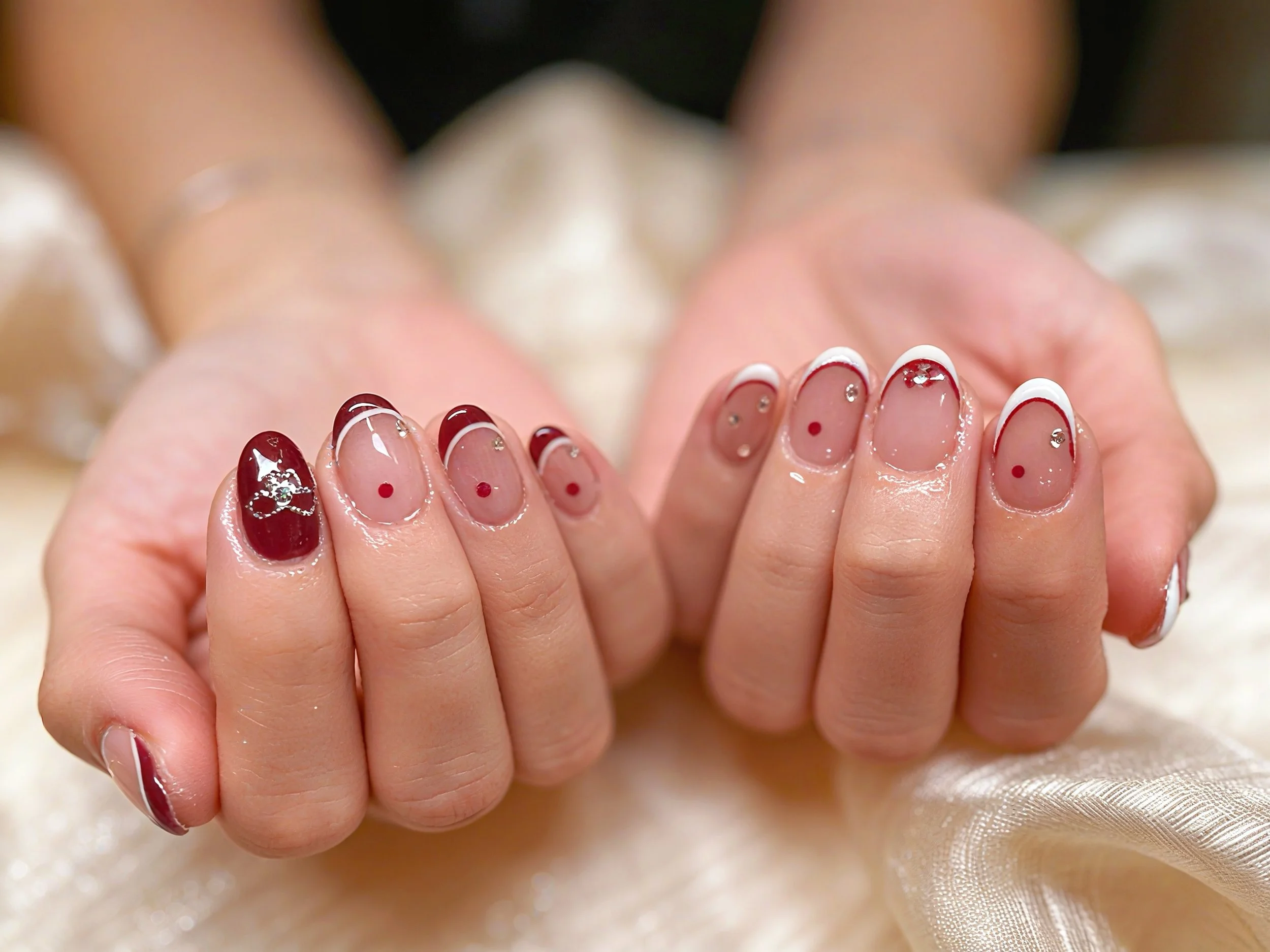 Close-up of hands with decorated manicured nails featuring red and white polish with small rhinestones and polka dots