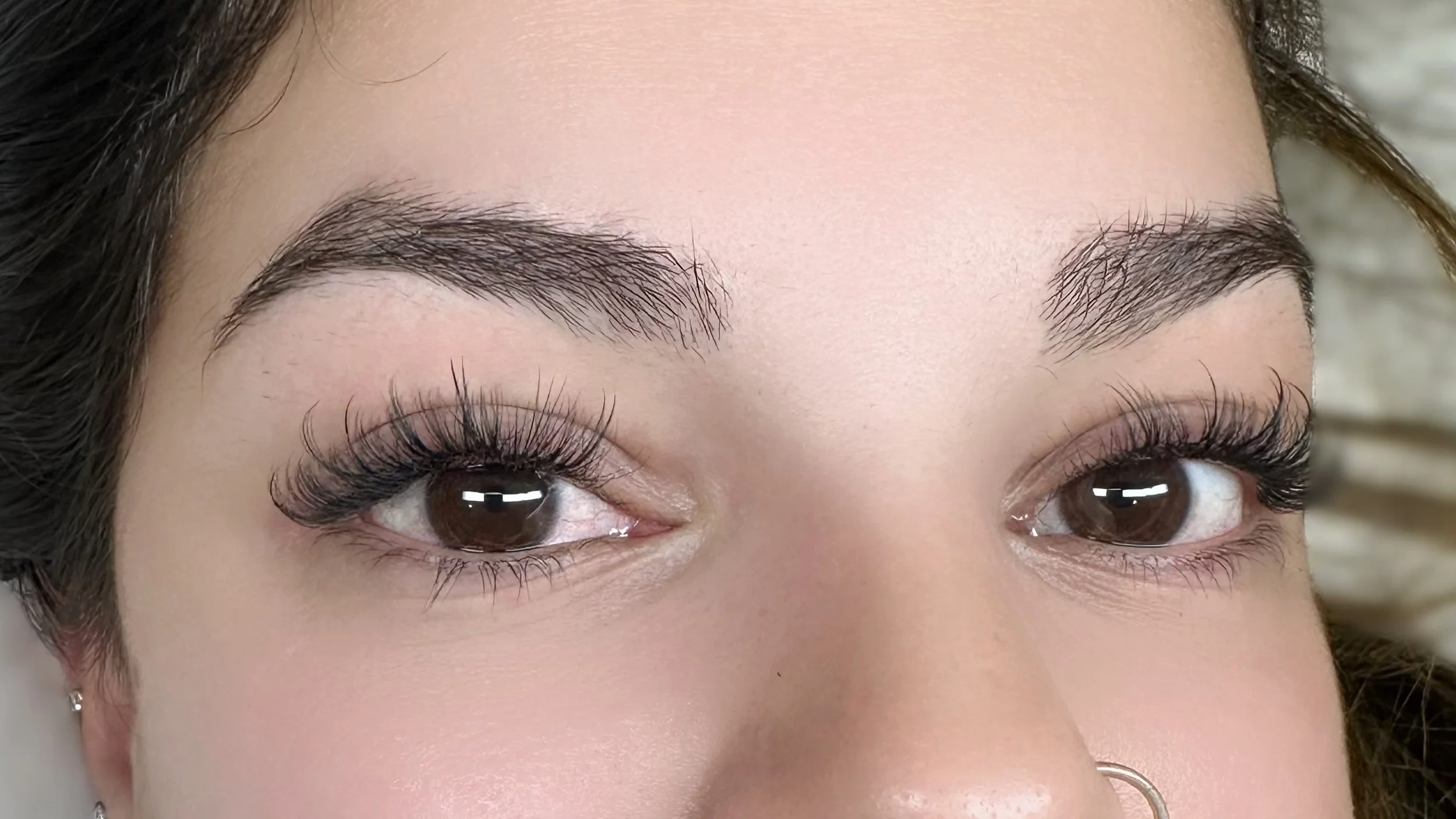Close-up of a woman's face showing her brown eyes, shaped eyebrows, and long, thick eyelashes.