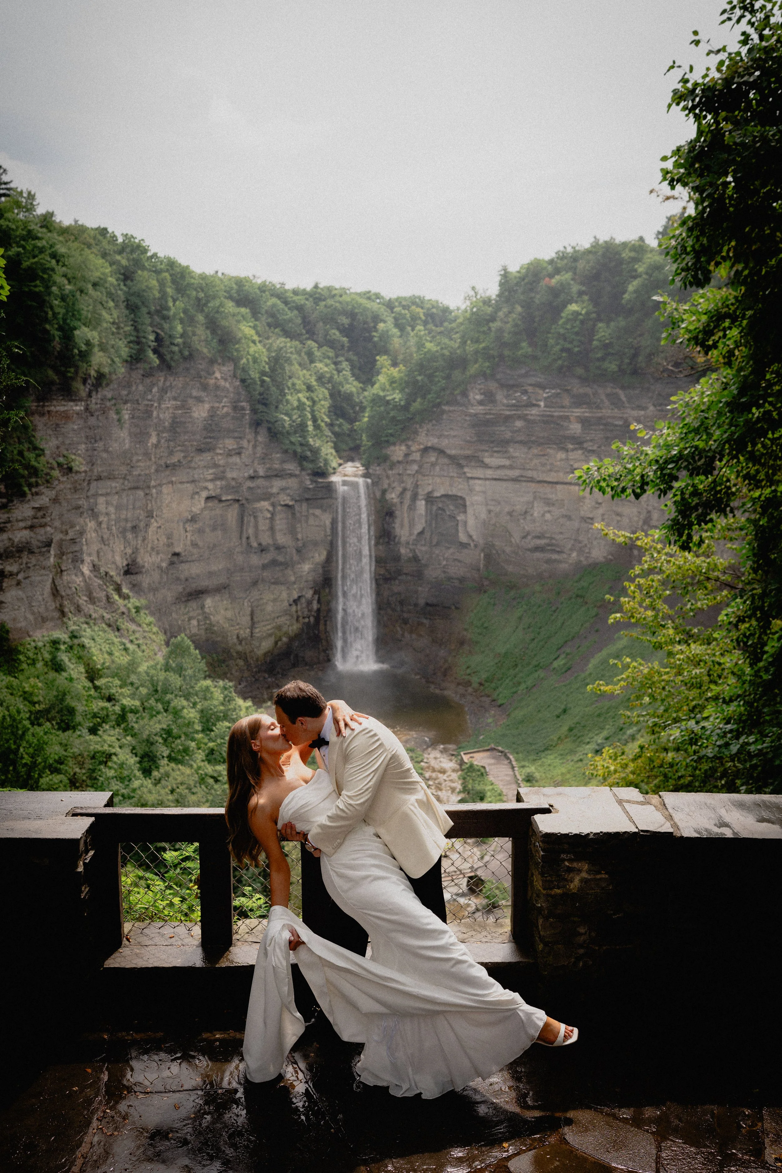 Luxury wedding photography portrait of a bride and groom kissing at a scenic Upstate New York waterfall overlook.