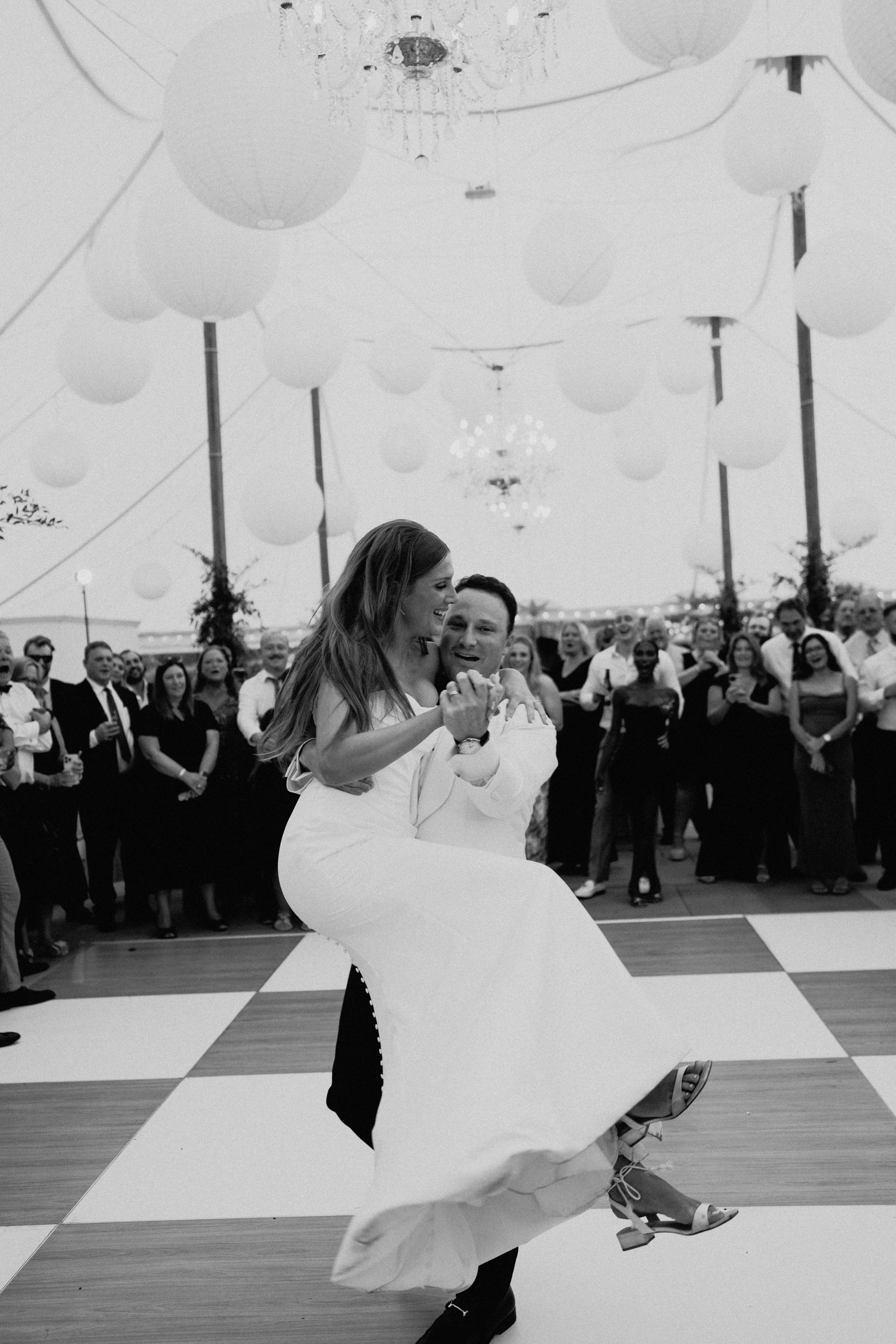 Black-and-white documentary wedding photography of the bride twirling on the dance floor as guests celebrate beneath the tent.