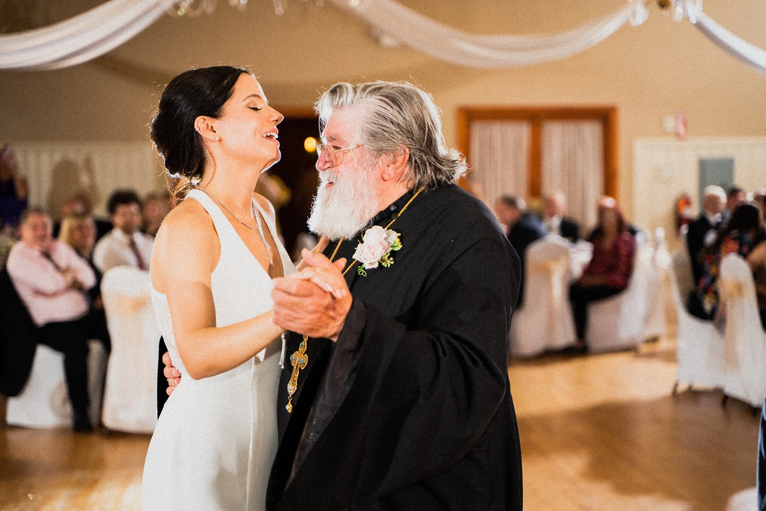 A bride and groom share a romantic dance together at their wedding reception, surrounded by joyful guests.
