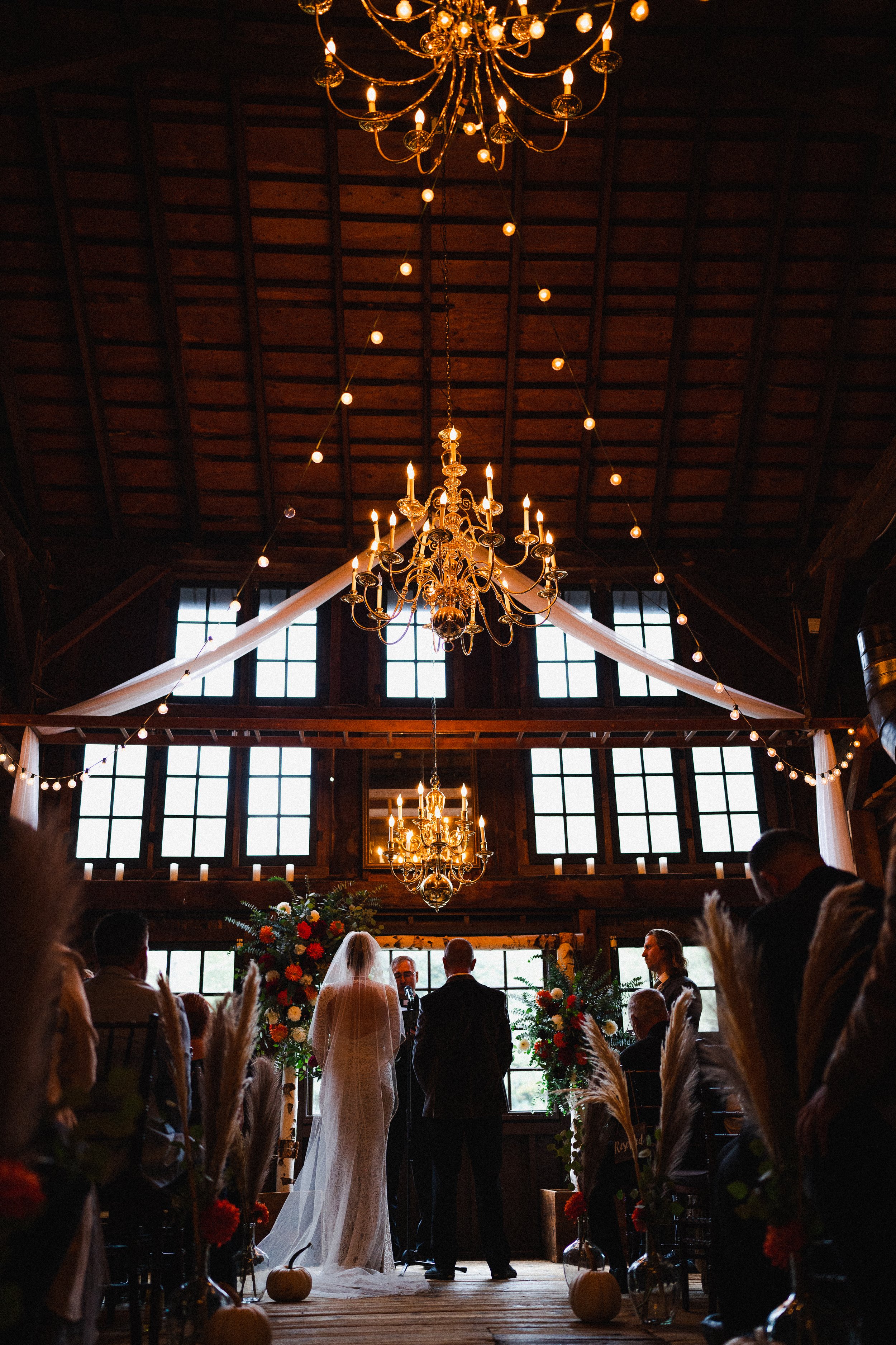 A wedding ceremony taking place inside a rustic barn, decorated with flowers and soft lighting for a romantic atmosphere.