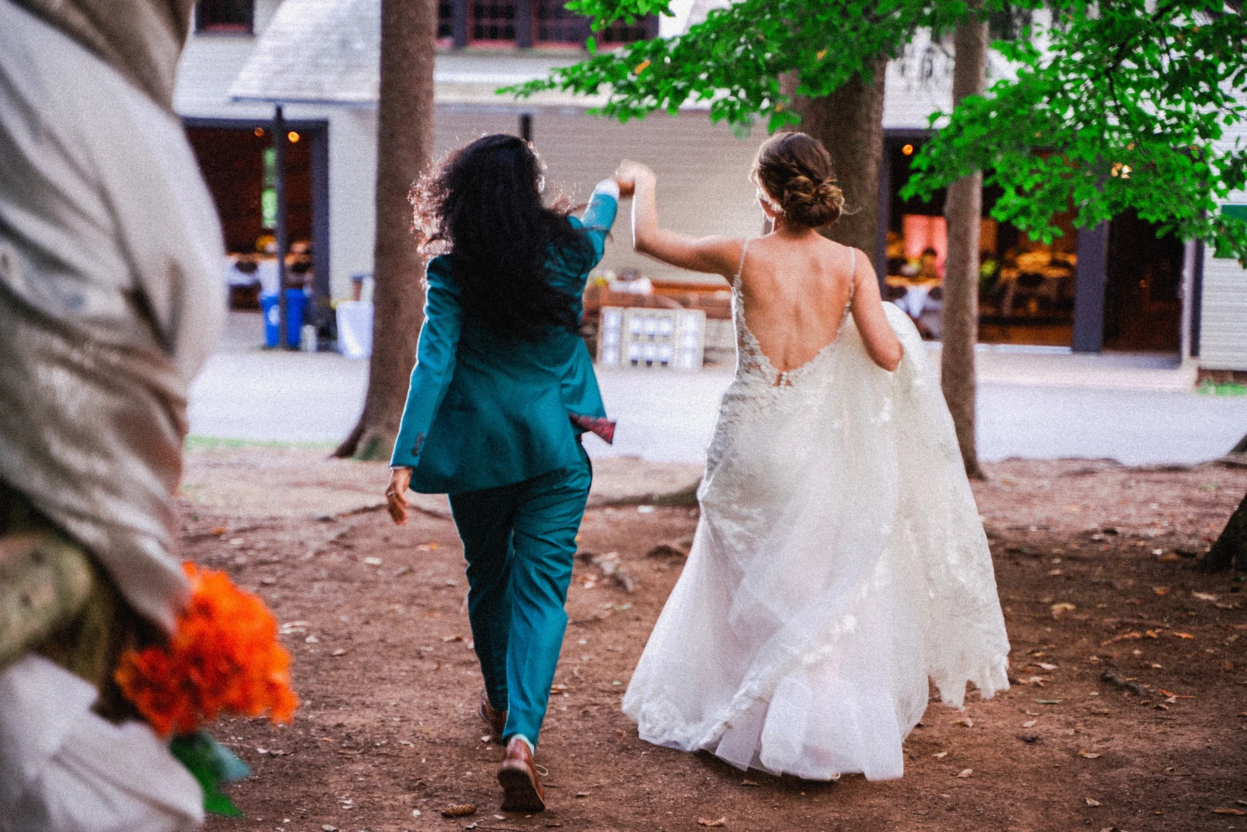 A bride and groom stroll hand in hand through a serene forest, surrounded by tall trees and dappled sunlight.