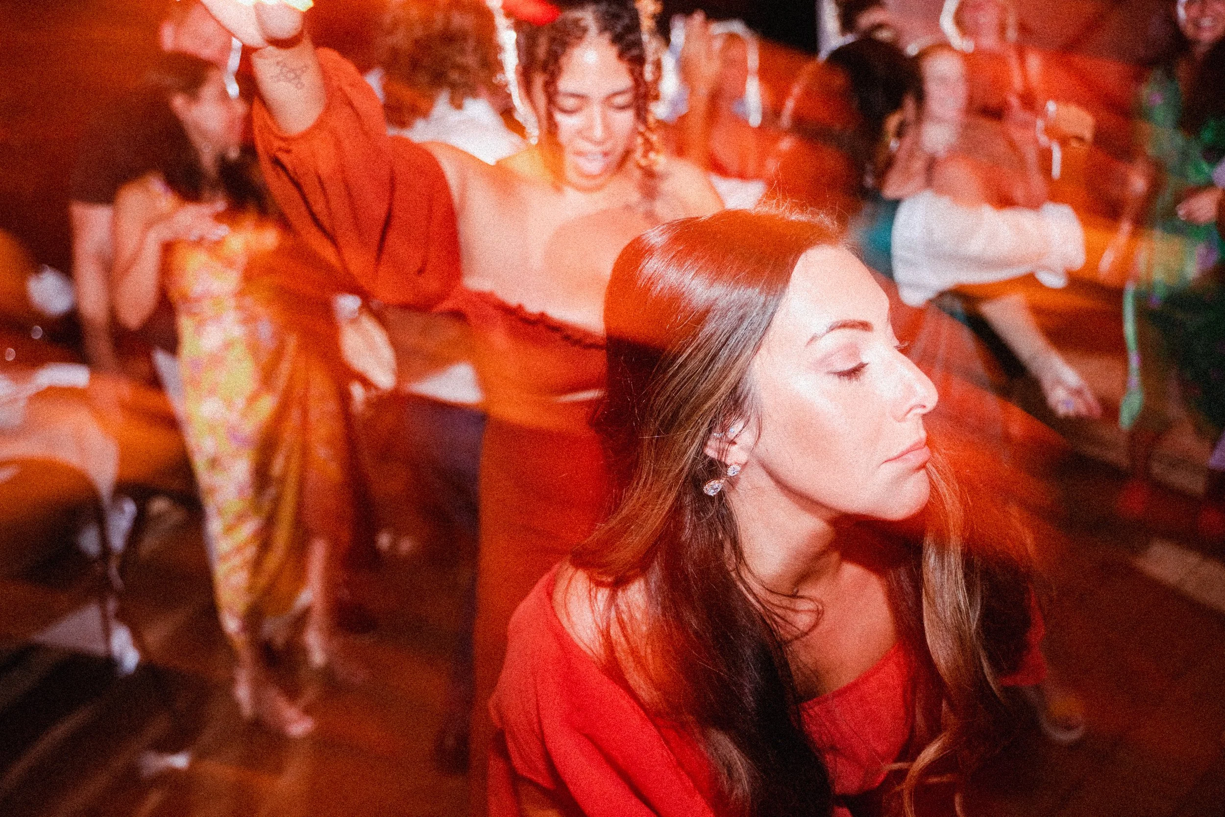 A woman in a vibrant red dress joyfully dancing at a lively party, surrounded by colorful decorations and guests.