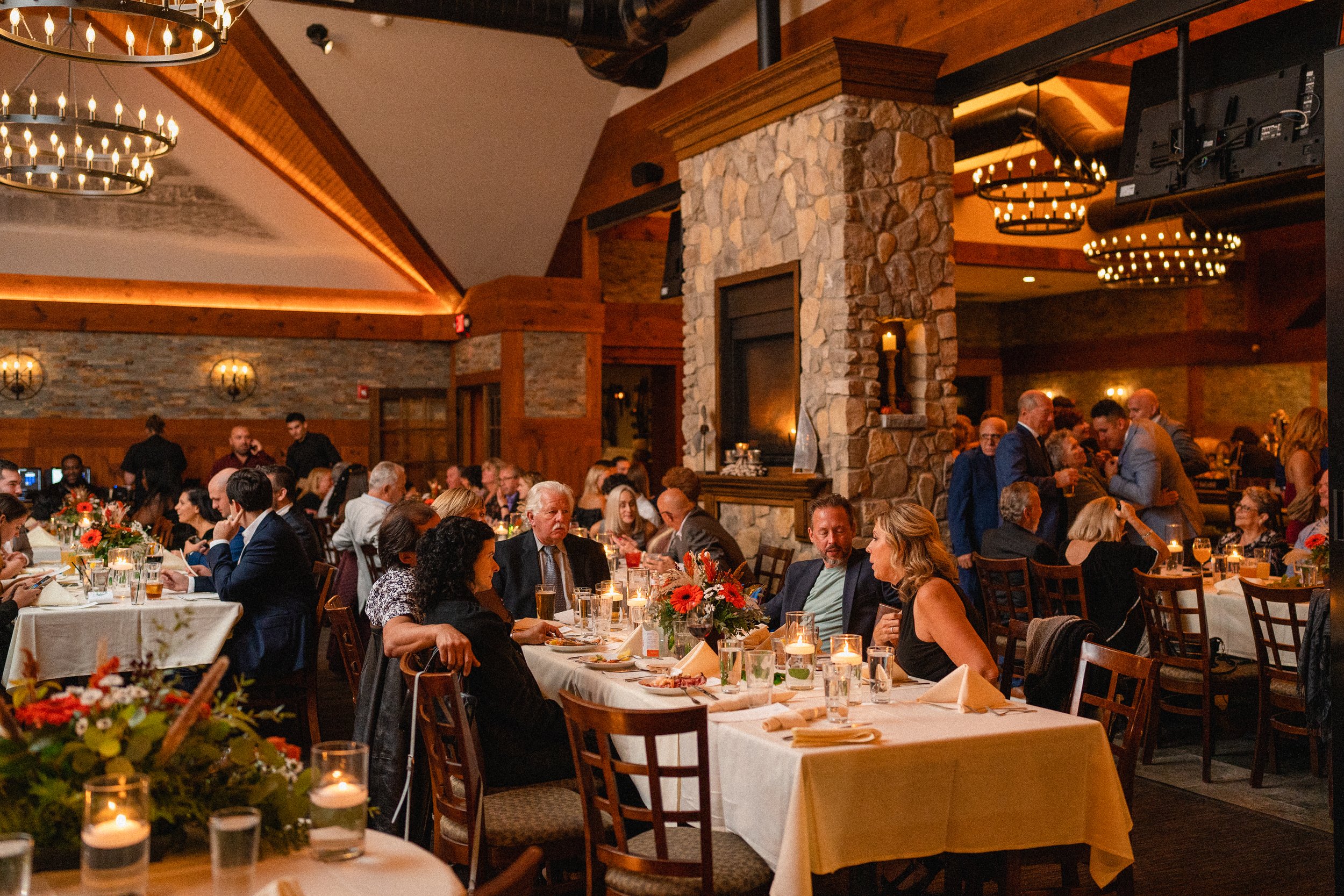 A large group of people dining at tables in a bustling restaurant, engaged in conversation and enjoying their meals.
