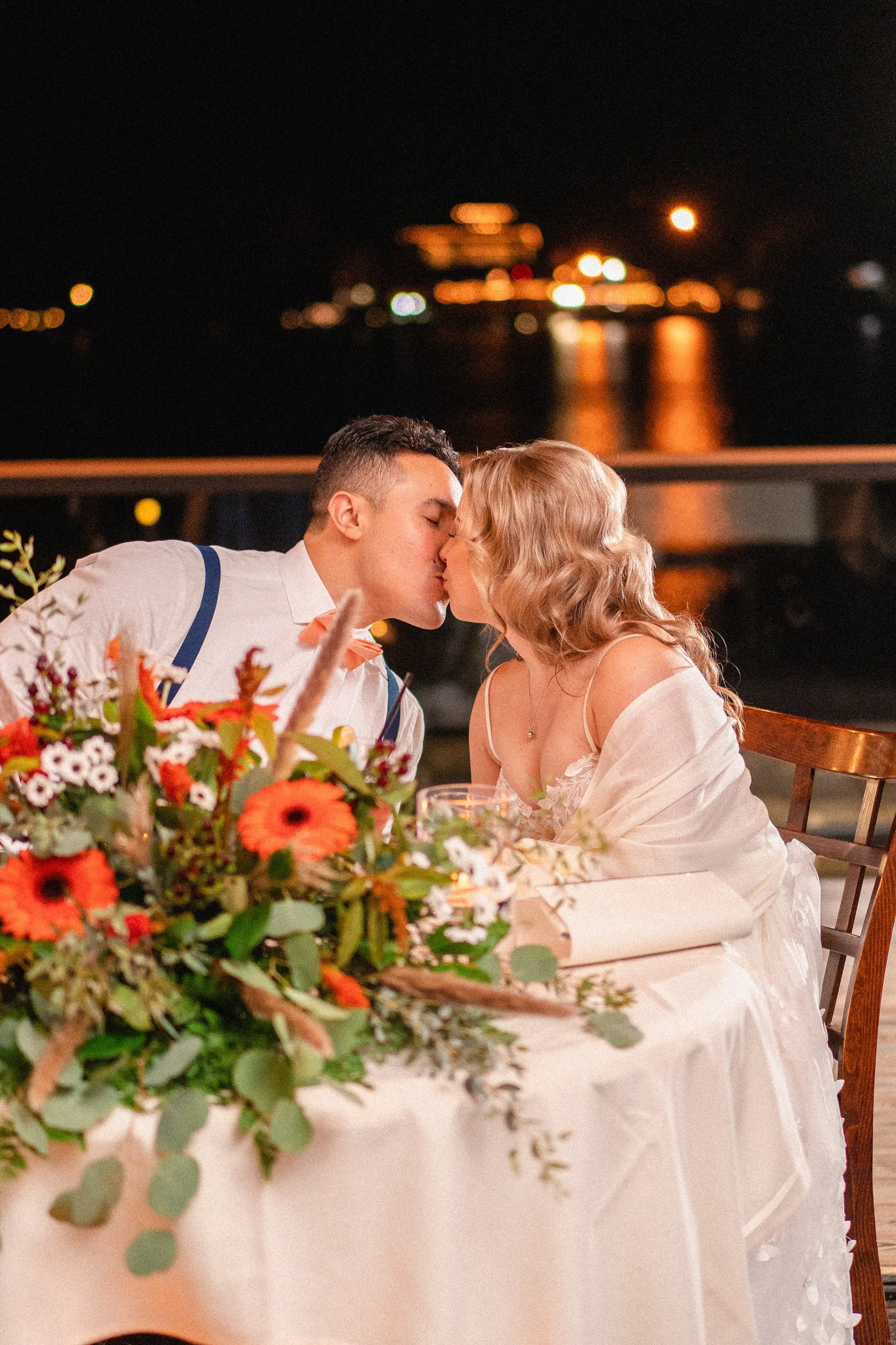 Couple sharing a romantic kiss during their wedding reception, surrounded by festive decorations and joyful guests.