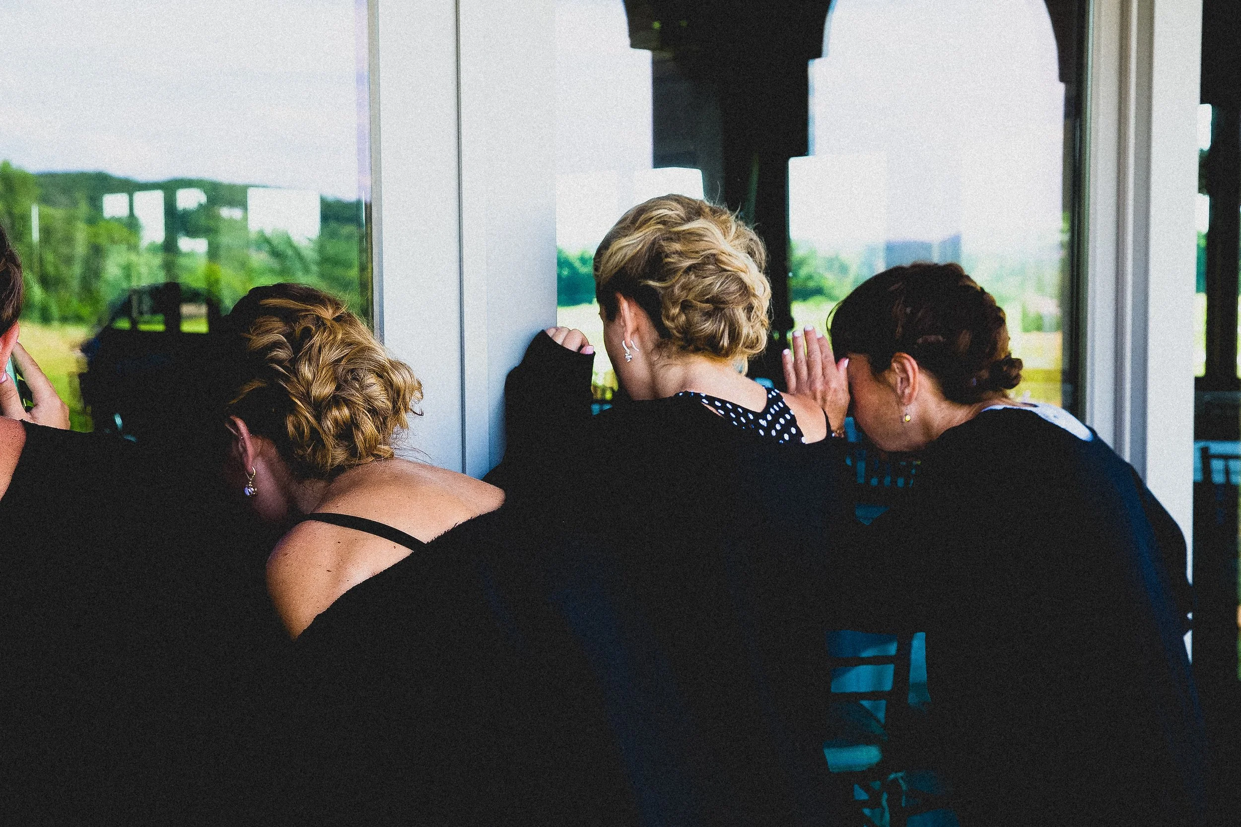 Three women gazing out a window, admiring a scenic view together.