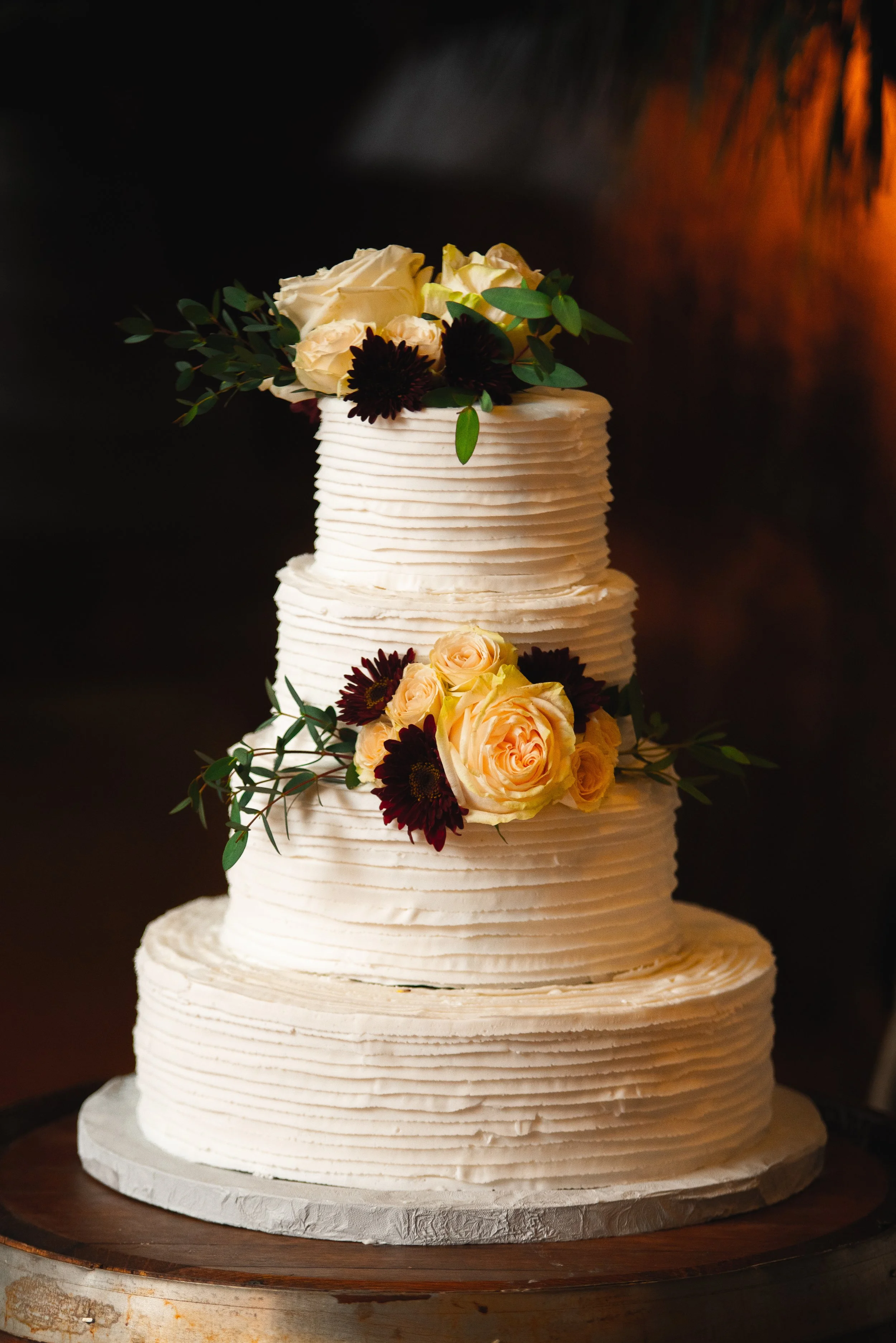 A three-tiered wedding cake adorned with colorful flowers, elegantly displayed on a decorative stand.