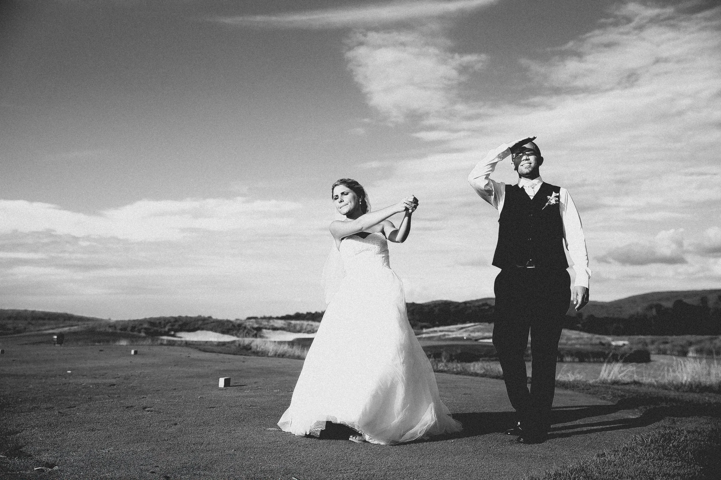 A bride and groom stand together on a lush green golf course, smiling and enjoying their wedding day.