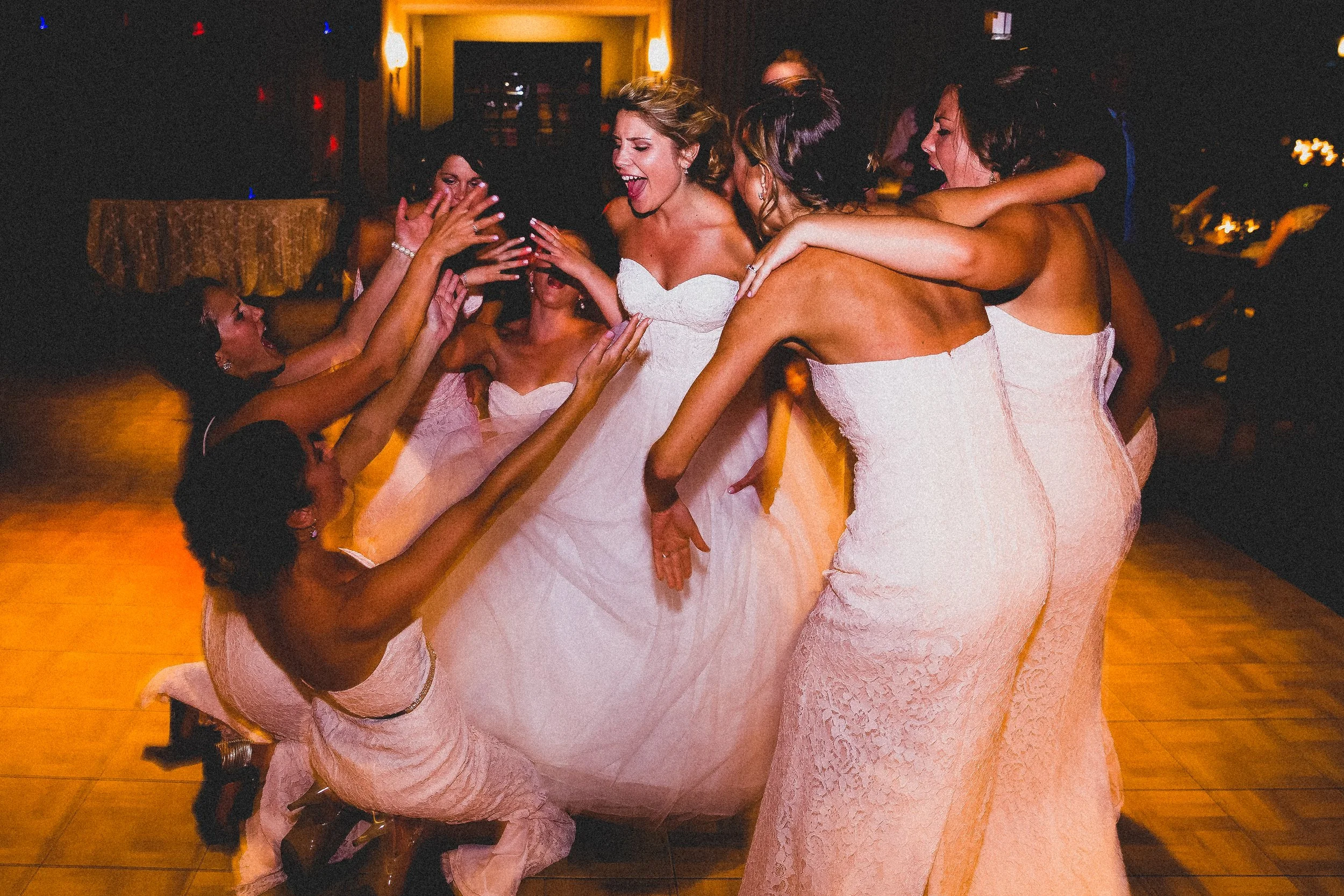 Bride joyfully dances with her bridesmaids at a lively wedding reception, surrounded by festive decorations and guests.