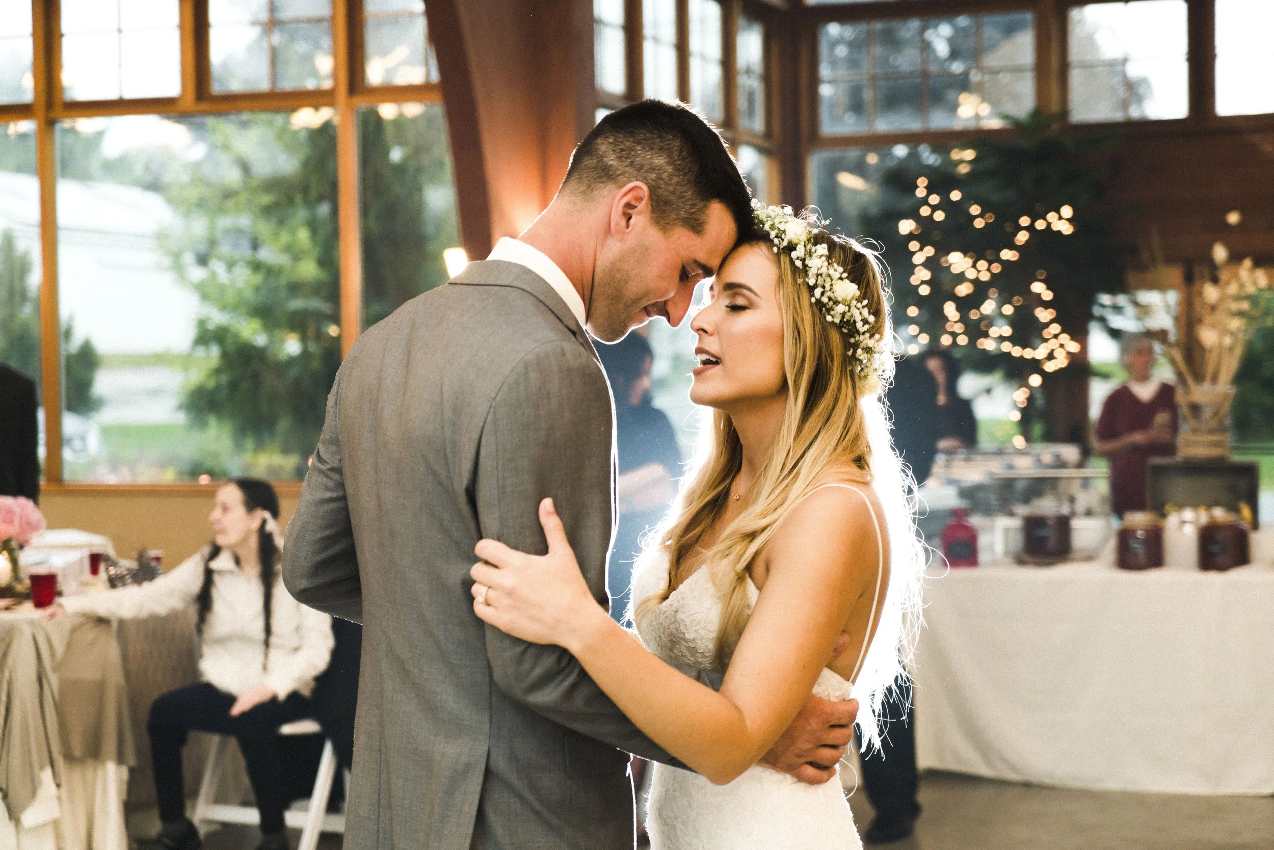 A bride and groom share a romantic first dance at their wedding reception, surrounded by joyful guests and soft lighting.