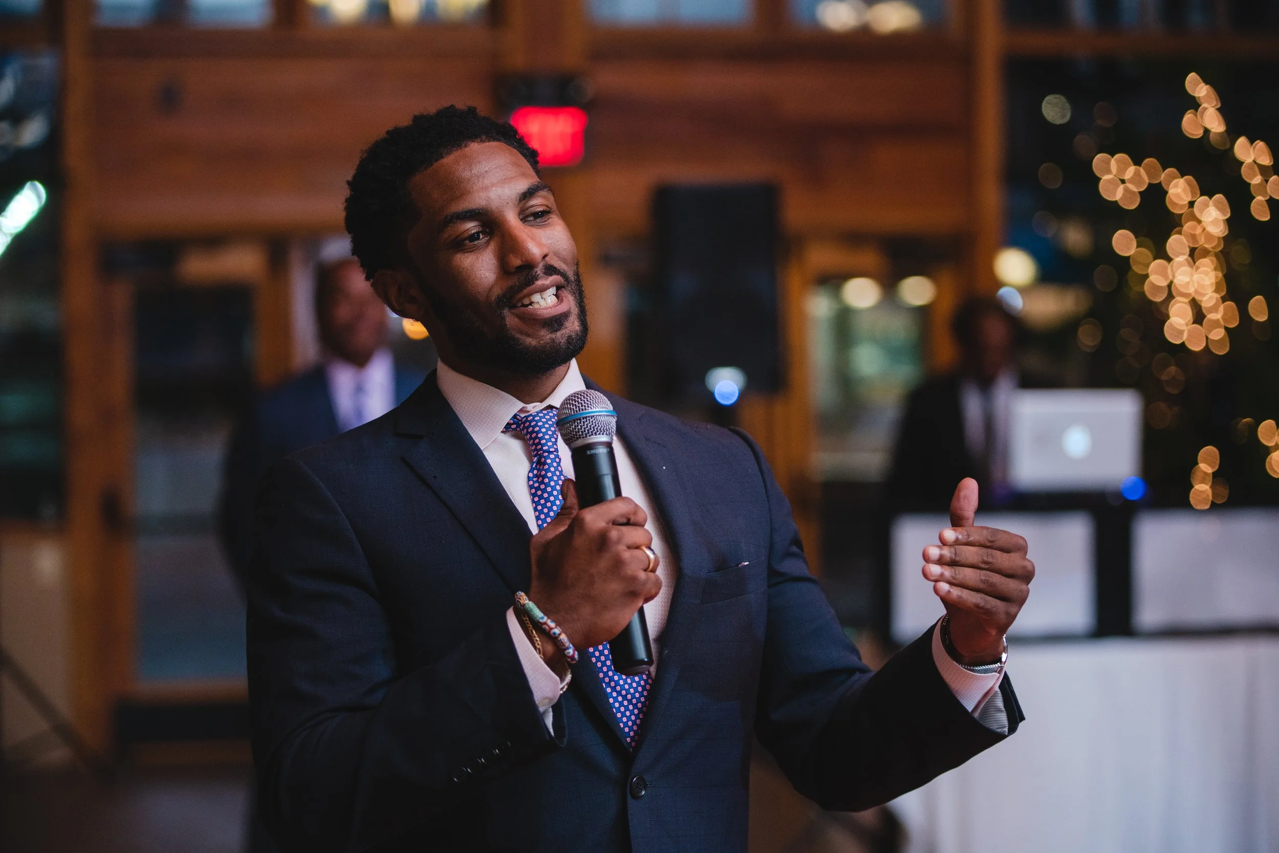 A man in a suit and tie delivers a speech into a microphone at a formal event.