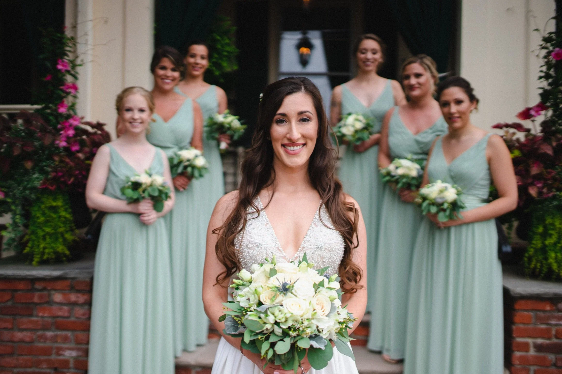 A bride and her bridesmaids smile together for a joyful group photo, showcasing their elegant dresses and floral arrangements.