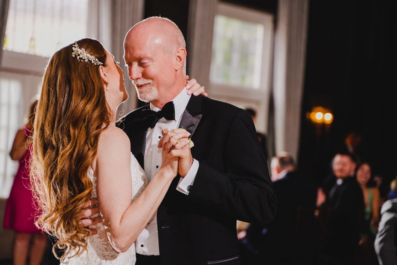 A bride and groom share their first dance, surrounded by soft lighting and joyful guests at their wedding reception.