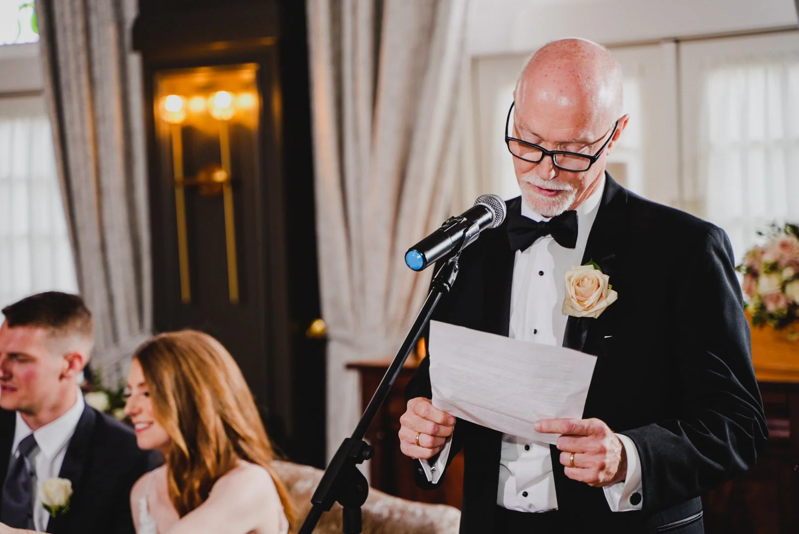 A man in a tuxedo delivers a heartfelt speech at a wedding ceremony, capturing the attention of the guests.