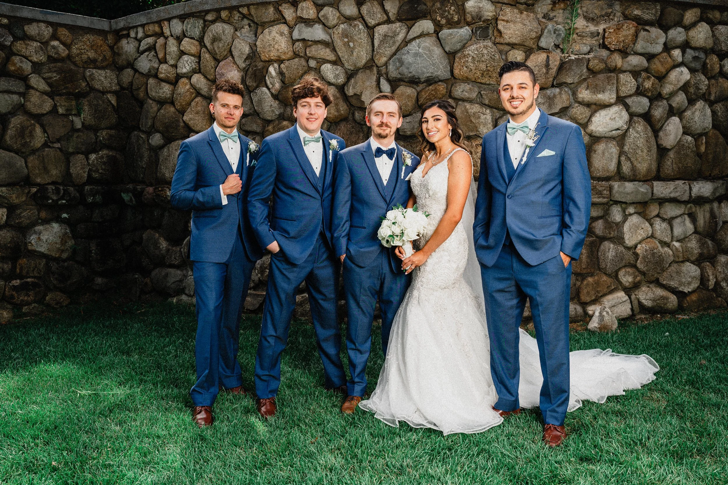 A bride and groom pose happily with their groomsmen, all dressed elegantly for the wedding celebration.