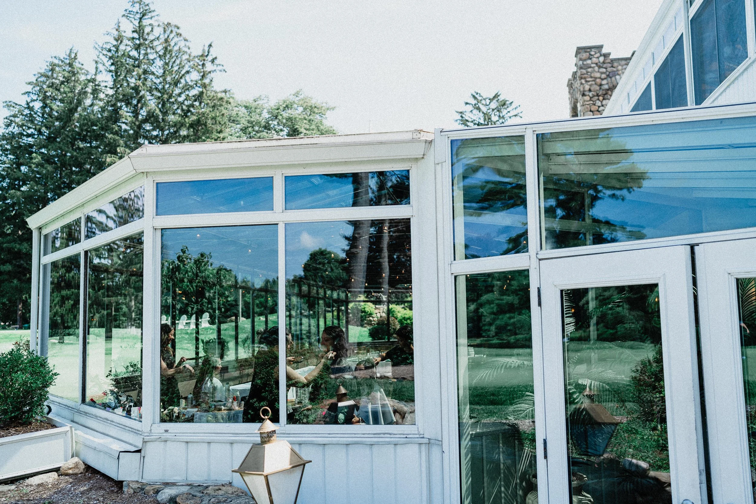 A wedding party gathers in a glassed patio area, enjoying the celebration surrounded by natural light.