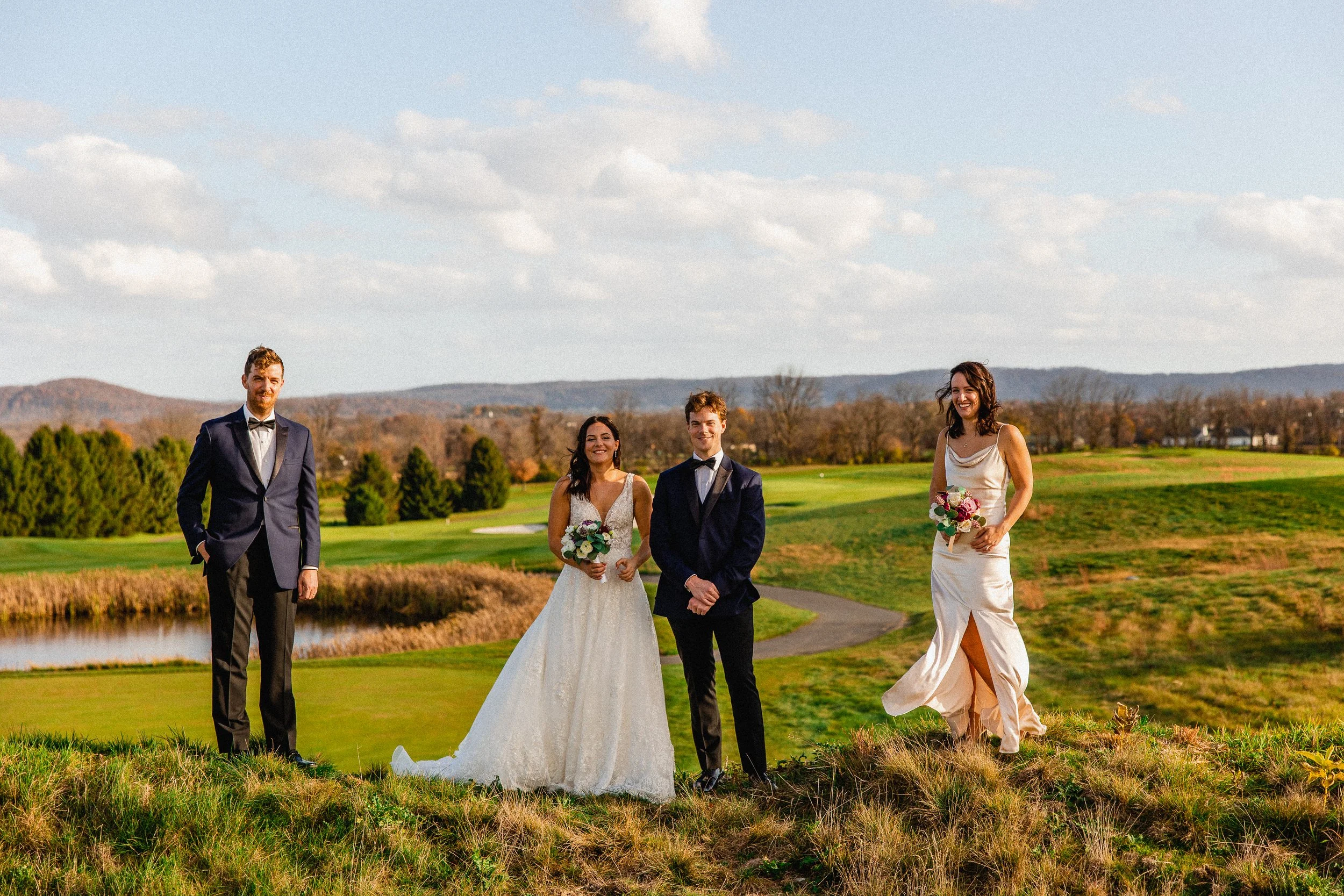 Bride and groom pose with their wedding party on a scenic golf course, surrounded by greenery and a clear blue sky.