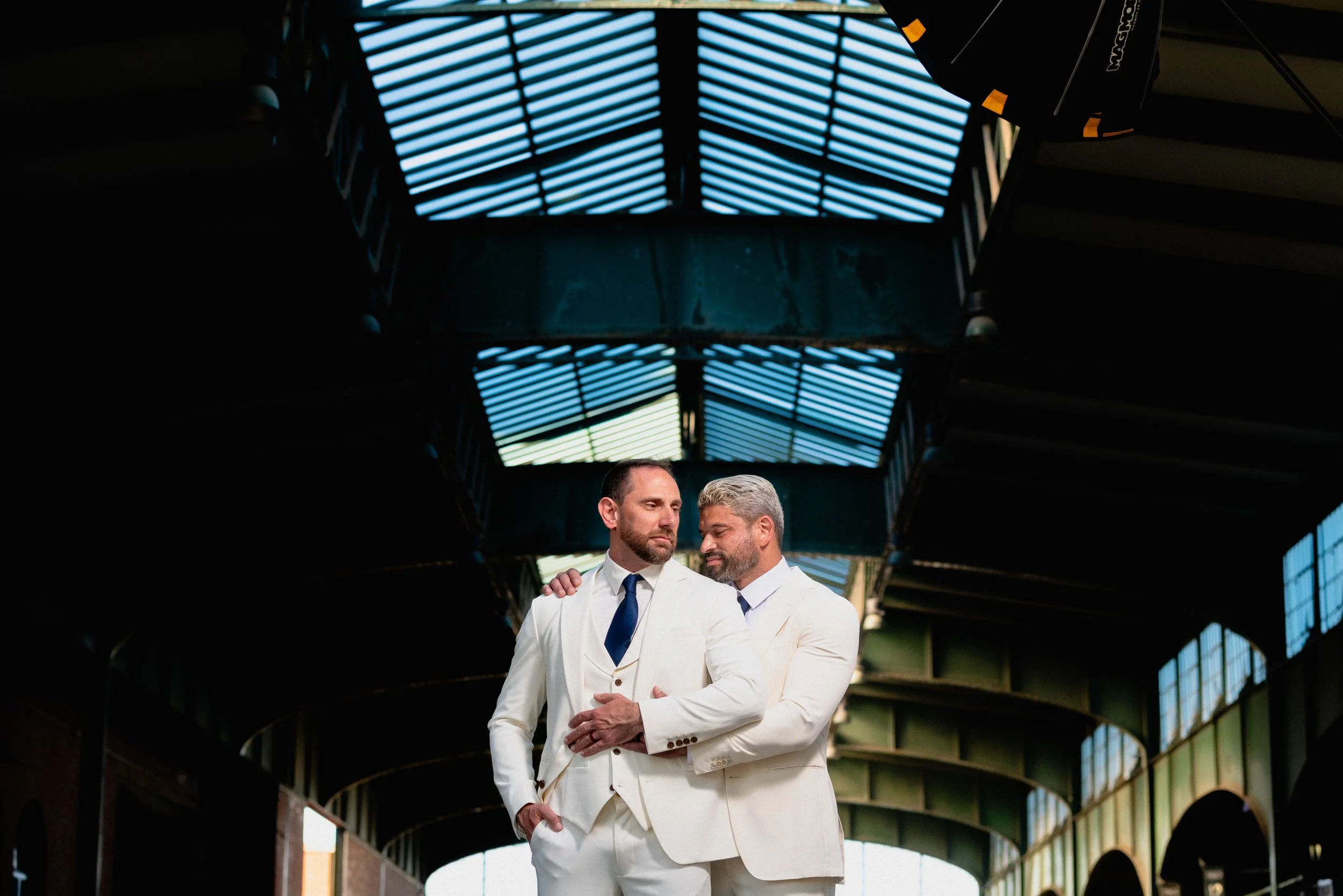 Two men in white suits stand in a narrow alleyway, surrounded by brick walls and dim lighting.