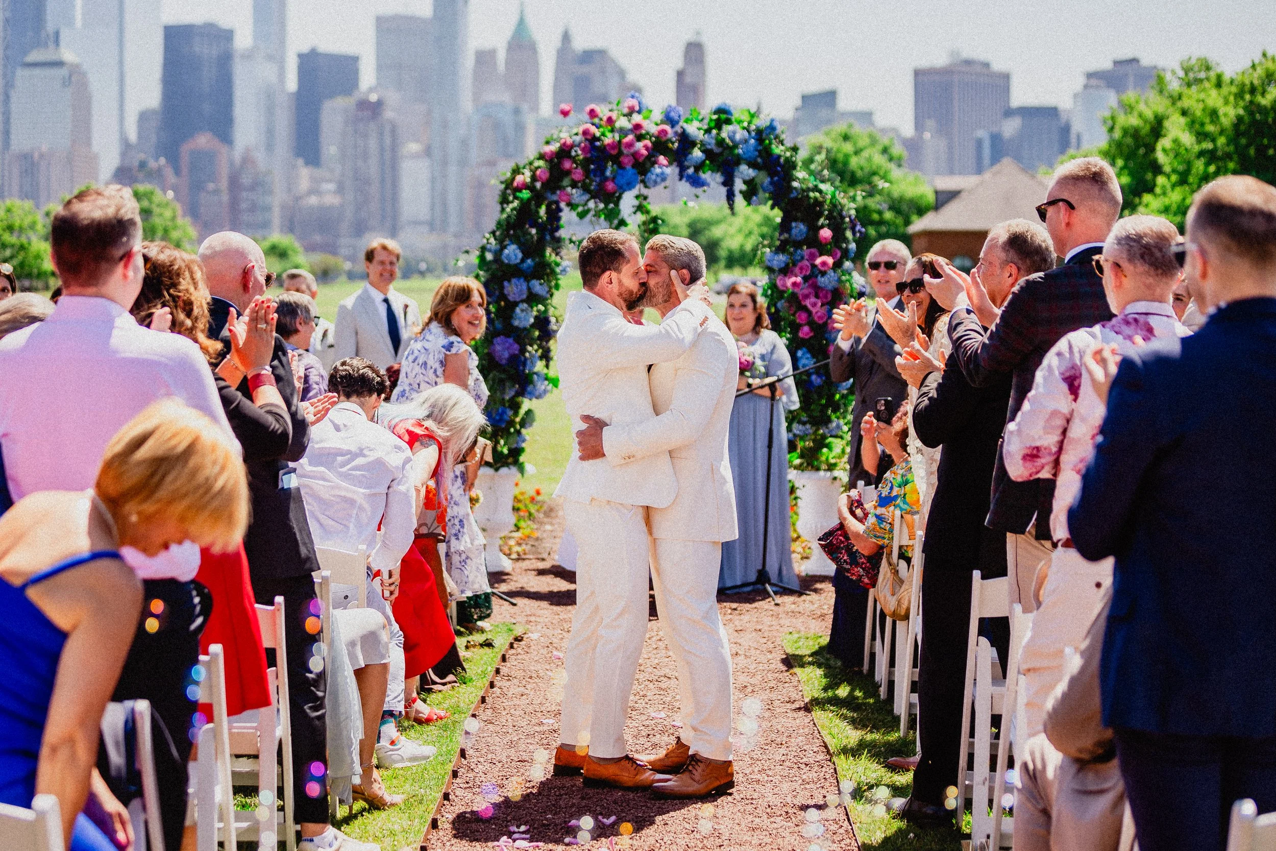 A joyful gay wedding celebration in New York City, featuring a couple exchanging vows with a skyline backdrop.