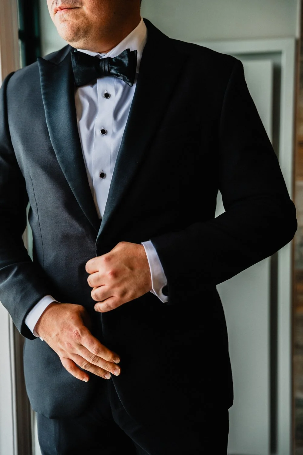 Close-up of a man in a black tuxedo with a white dress shirt and black bow tie, adjusting his jacket.