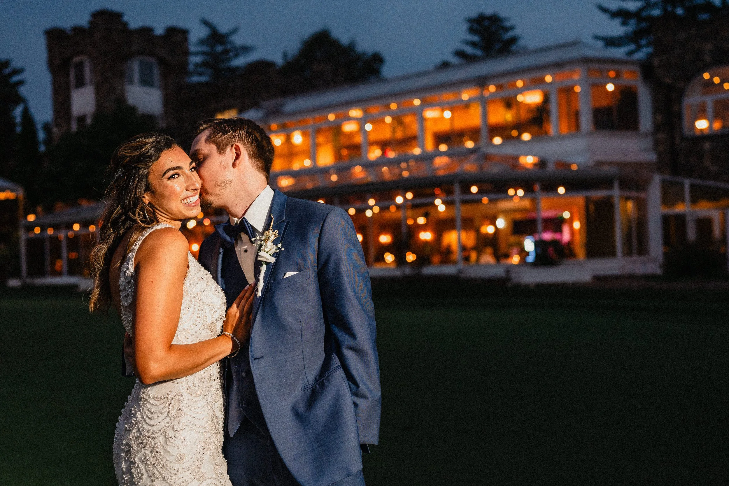 A newlywed couple dancing outdoors at night, with a large illuminated house in the background.