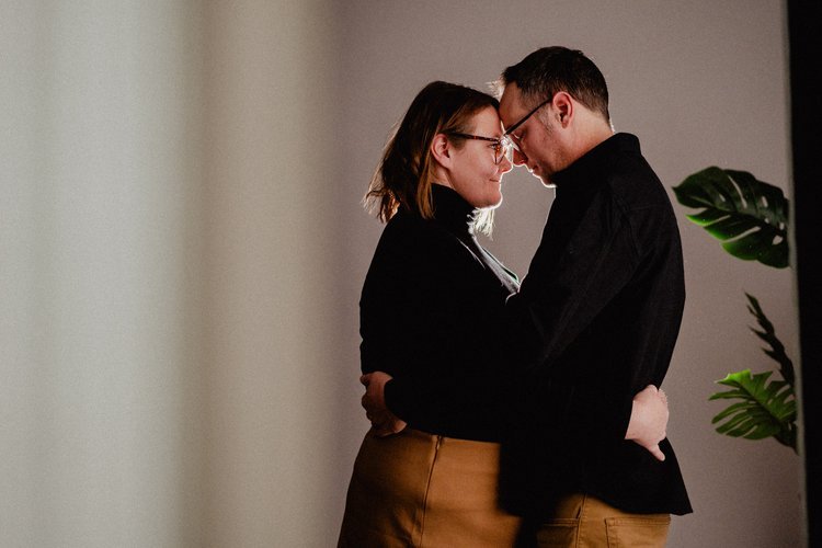 A couple embracing with foreheads touching in a dimly lit room.