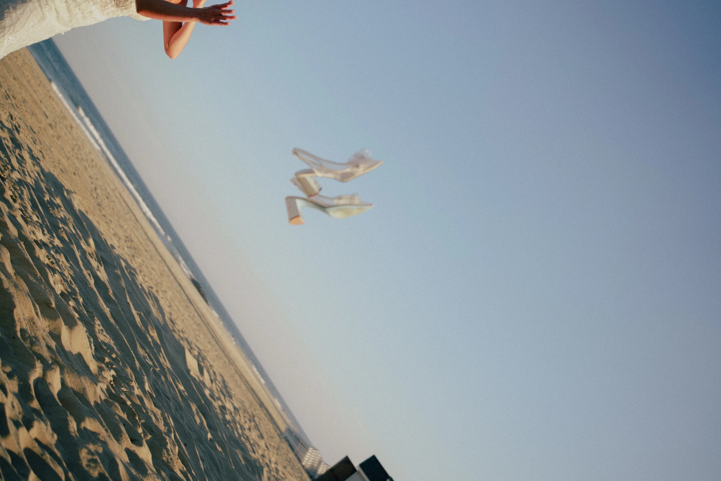 A woman in a white dress standing on a sandy beach holding her arms out at wave resort - Wedding photographers- Timeline Visuals