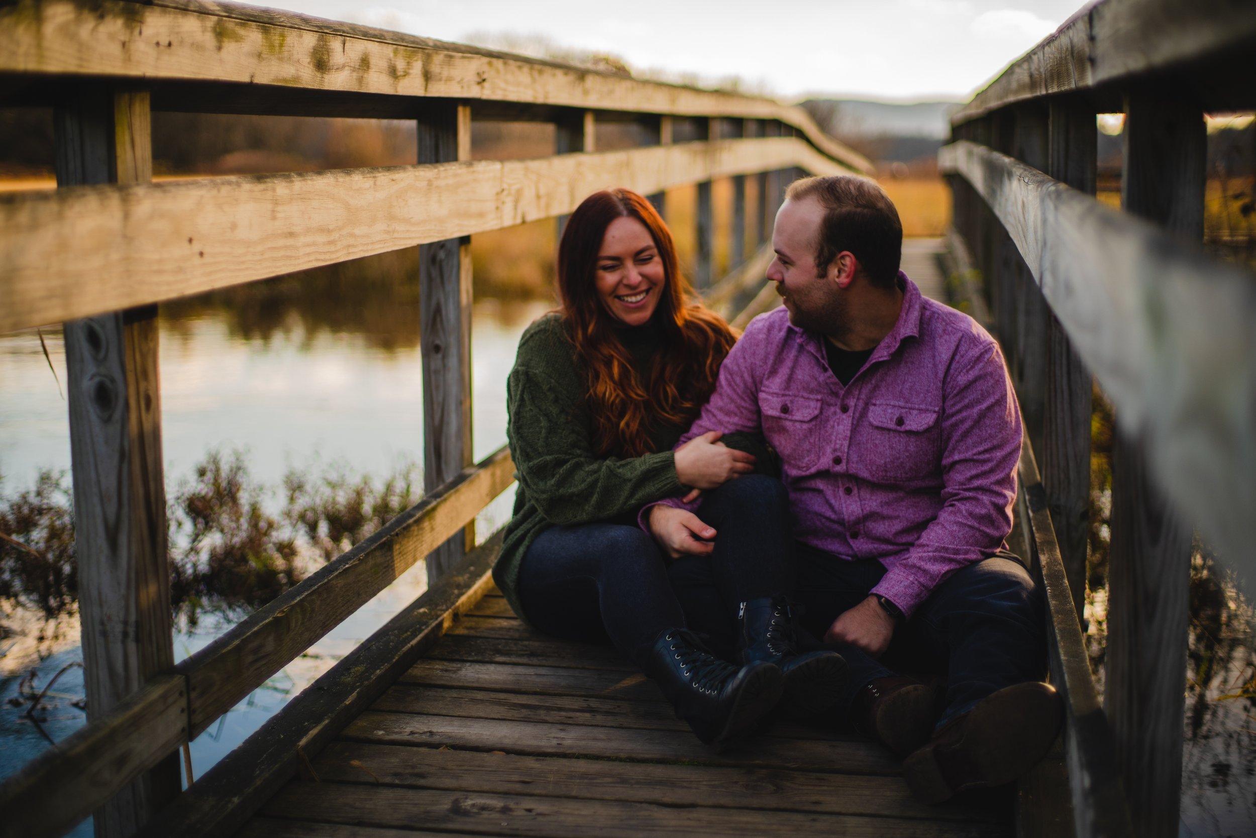 A couple sitting on a wooden dock near a body of water, smiling and enjoying each other's company during sunset.