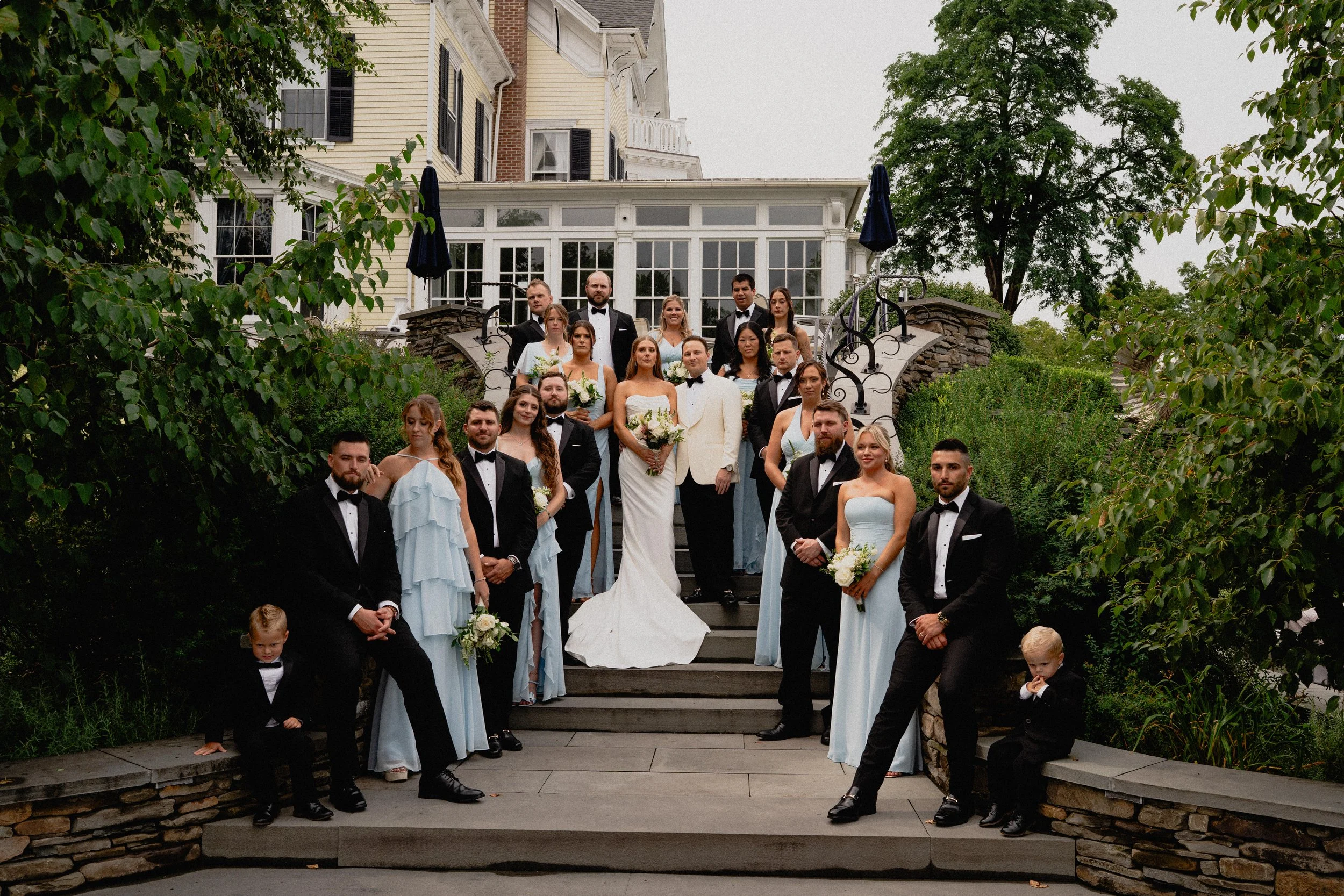 Documentary wedding photography of the bride, groom, and wedding party gathered on the steps of an Upstate New York estate.