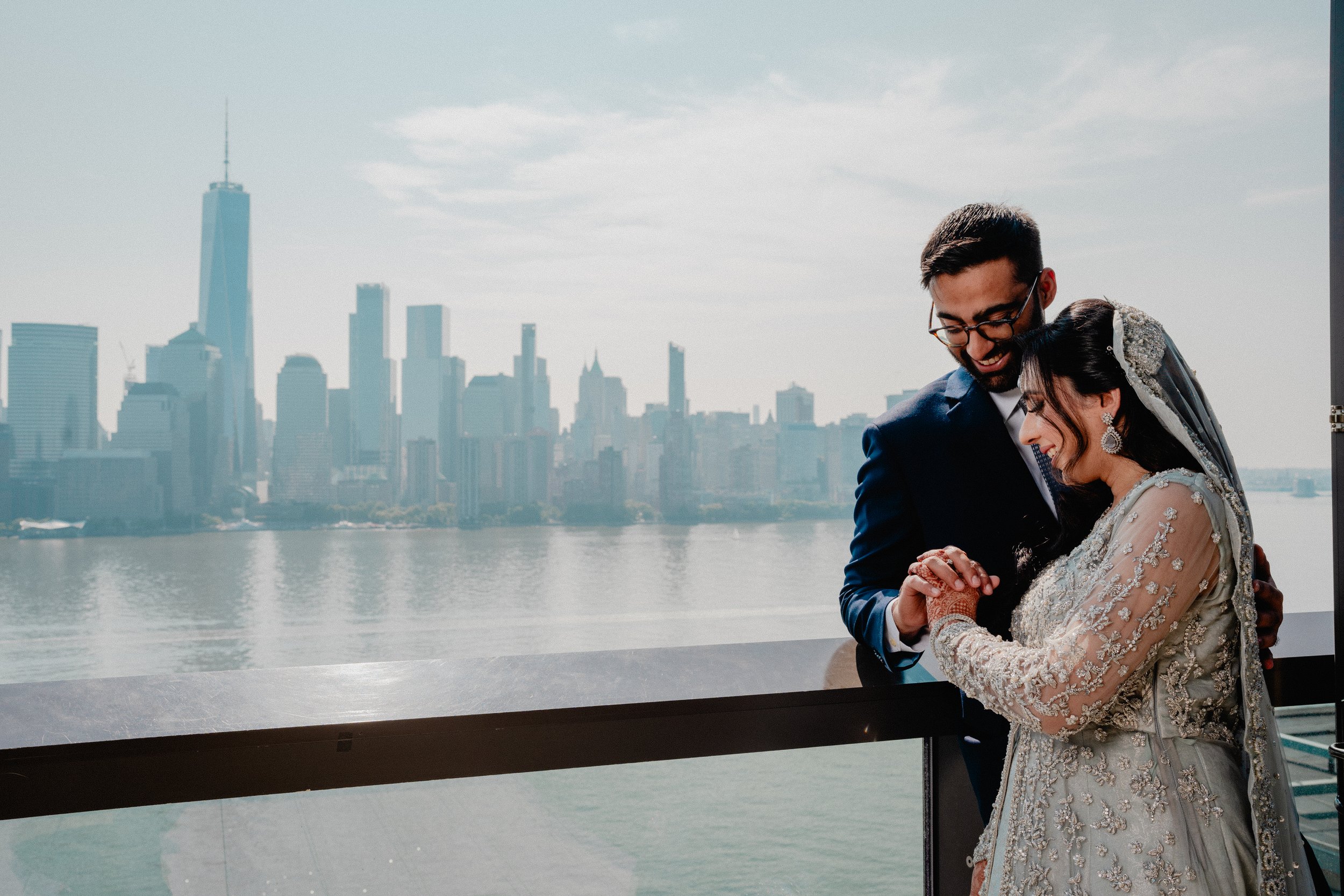 Luxury NJ wedding photography at Liberty House: a couple shares a quiet moment by a window overlooking the New York City skyline and river.