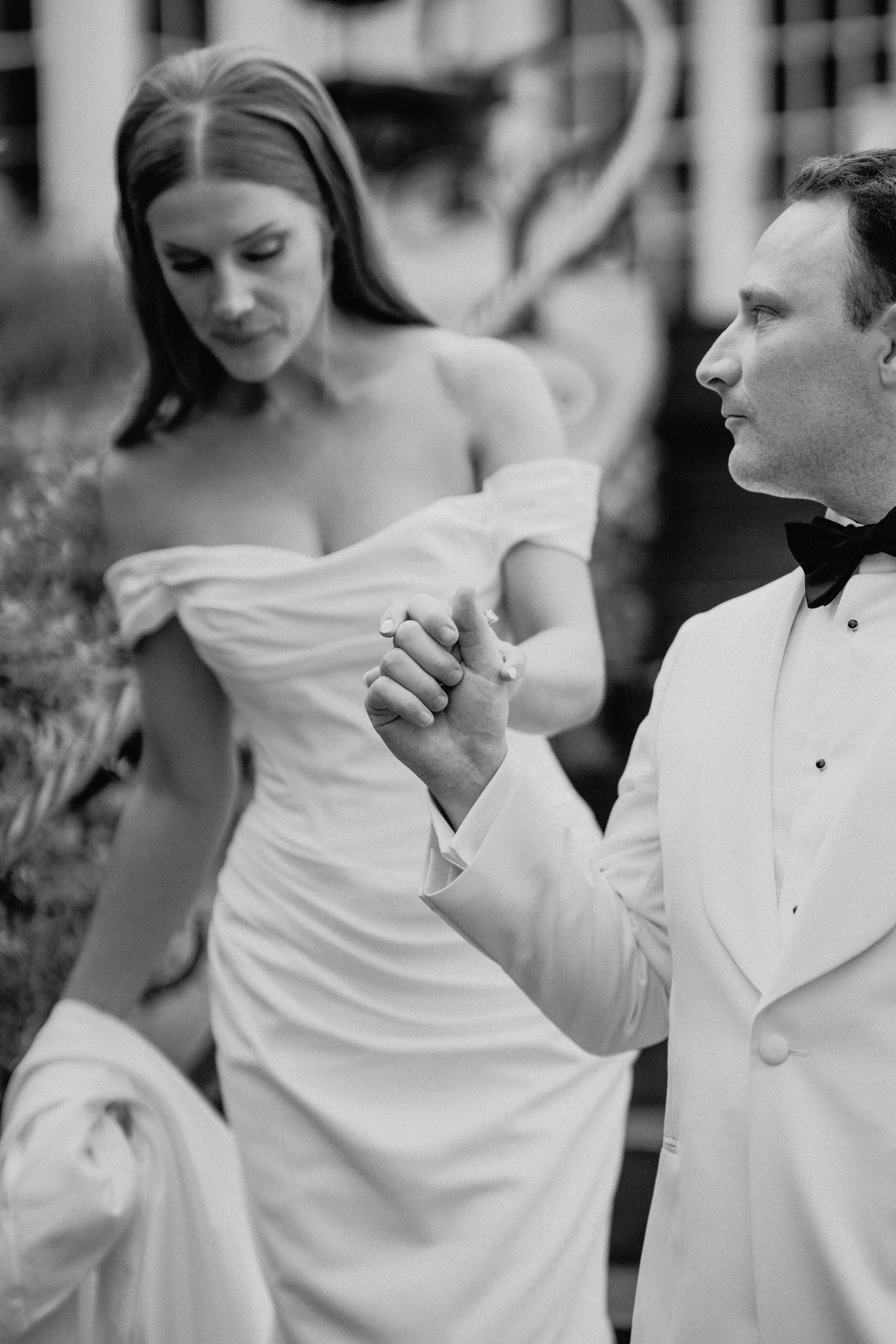 Black-and-white documentary wedding photography of a bride reading a card beside a man in a white dinner jacket.