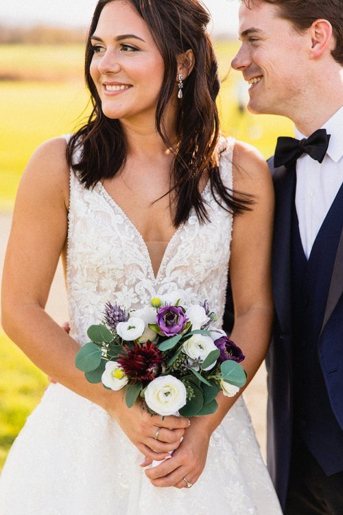 Bride holding a bouquet standing next to a groom outdoors during a wedding.