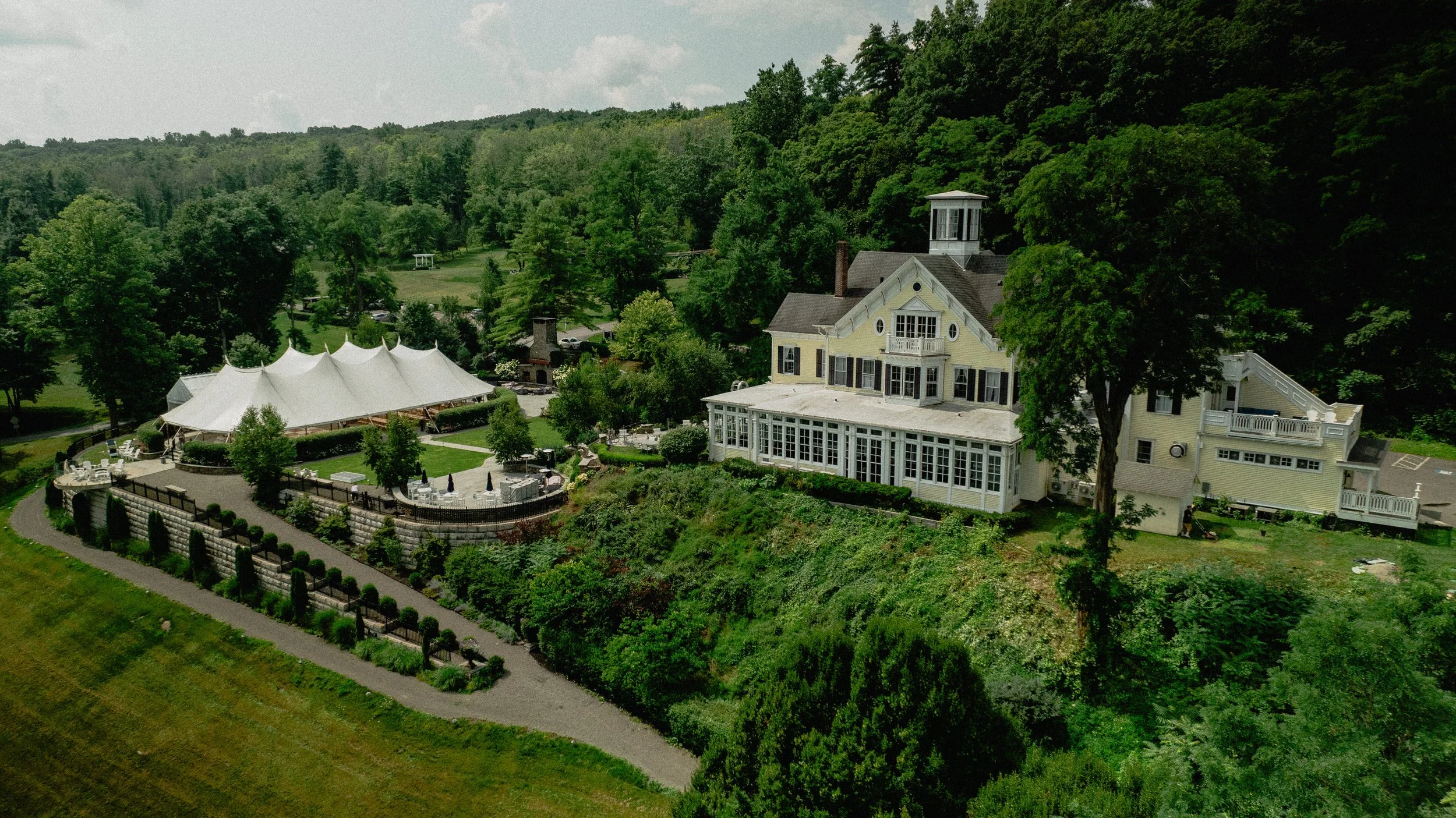 Luxury wedding photography aerial view of an Upstate New York estate and elegant tent surrounded by wooded hills.