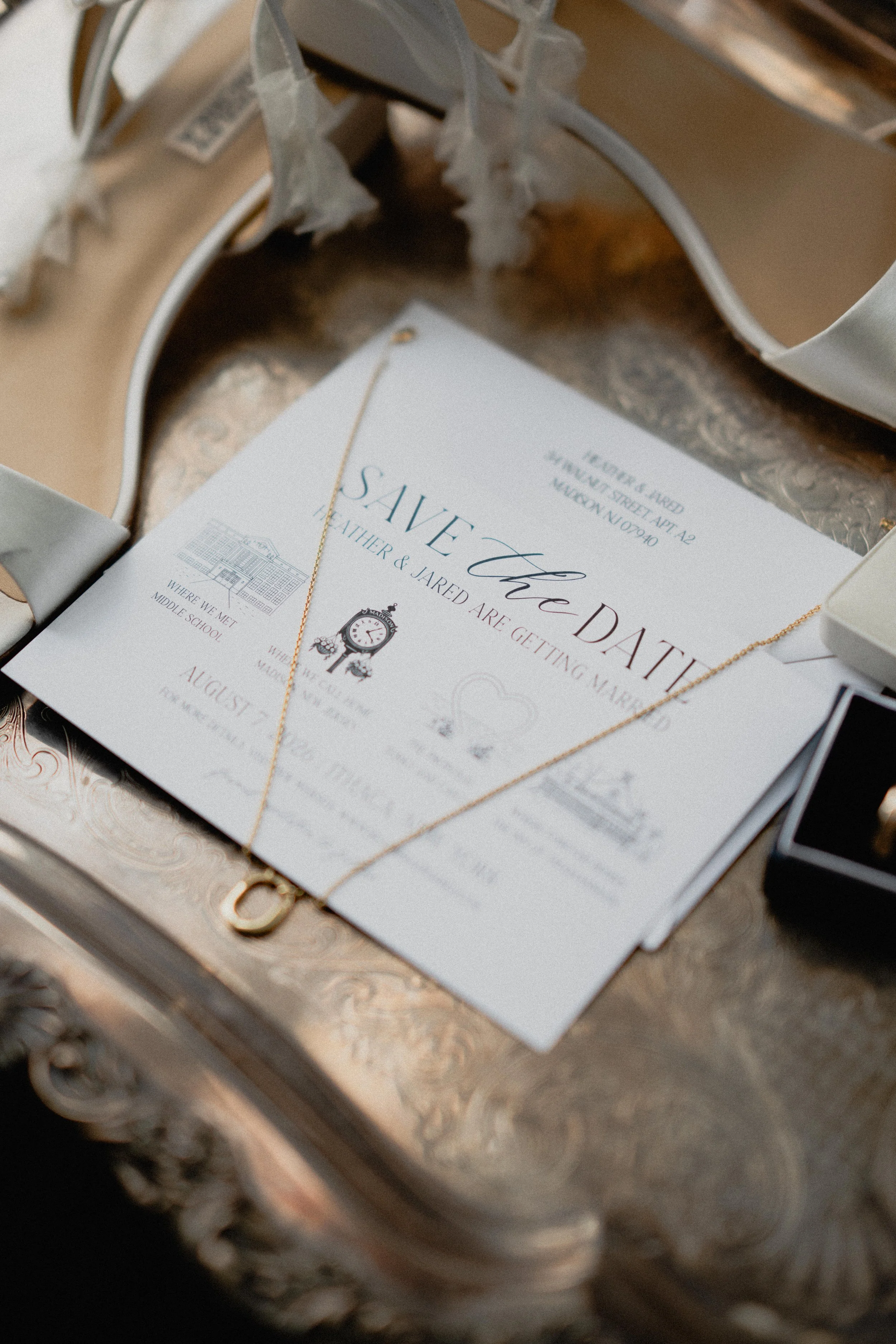 Editorial wedding photography detail of a save-the-date card and gold necklace arranged on an ornate silver tray.