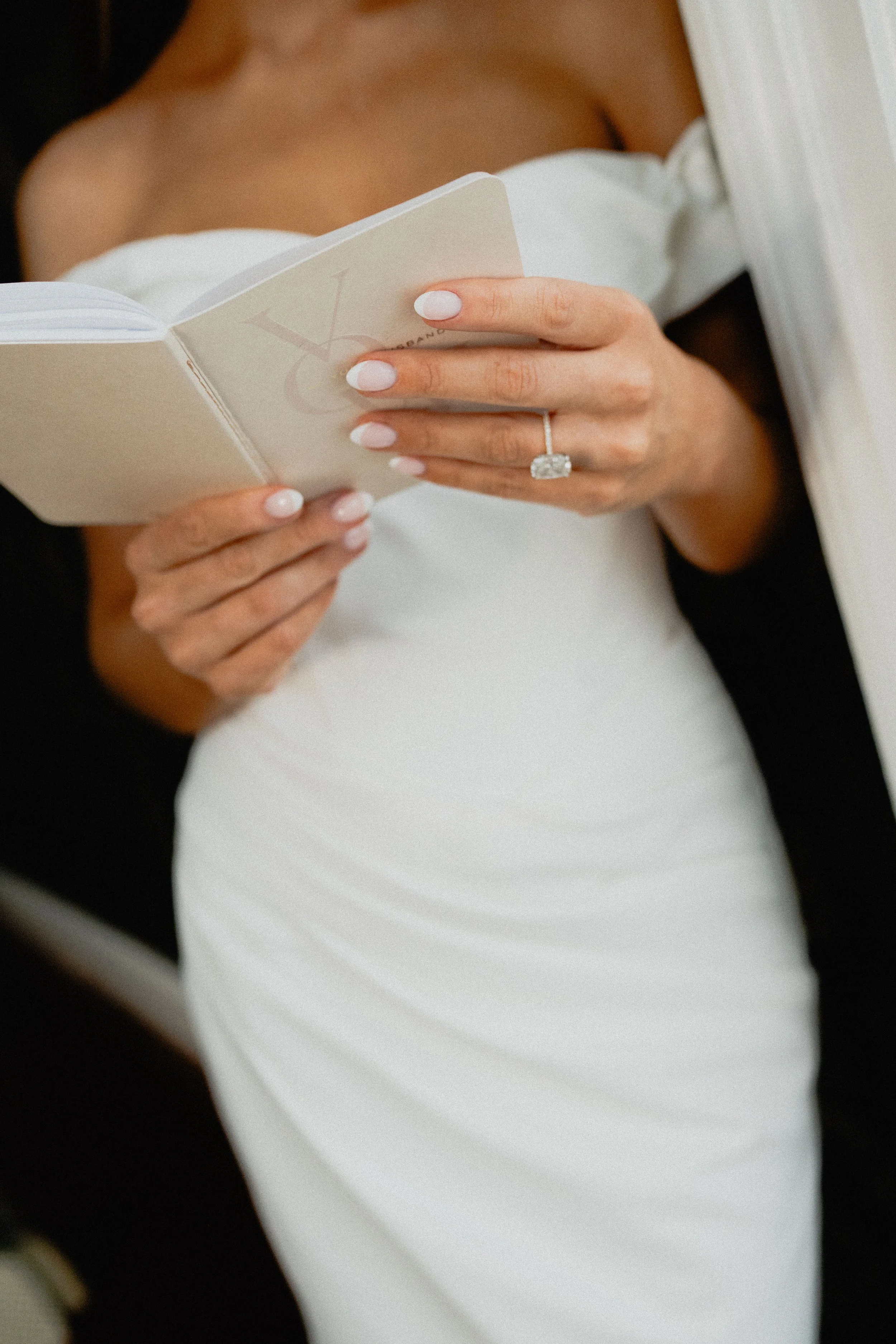 Editorial wedding photography close-up of a bride holding a card, with her engagement ring and manicure visible.
