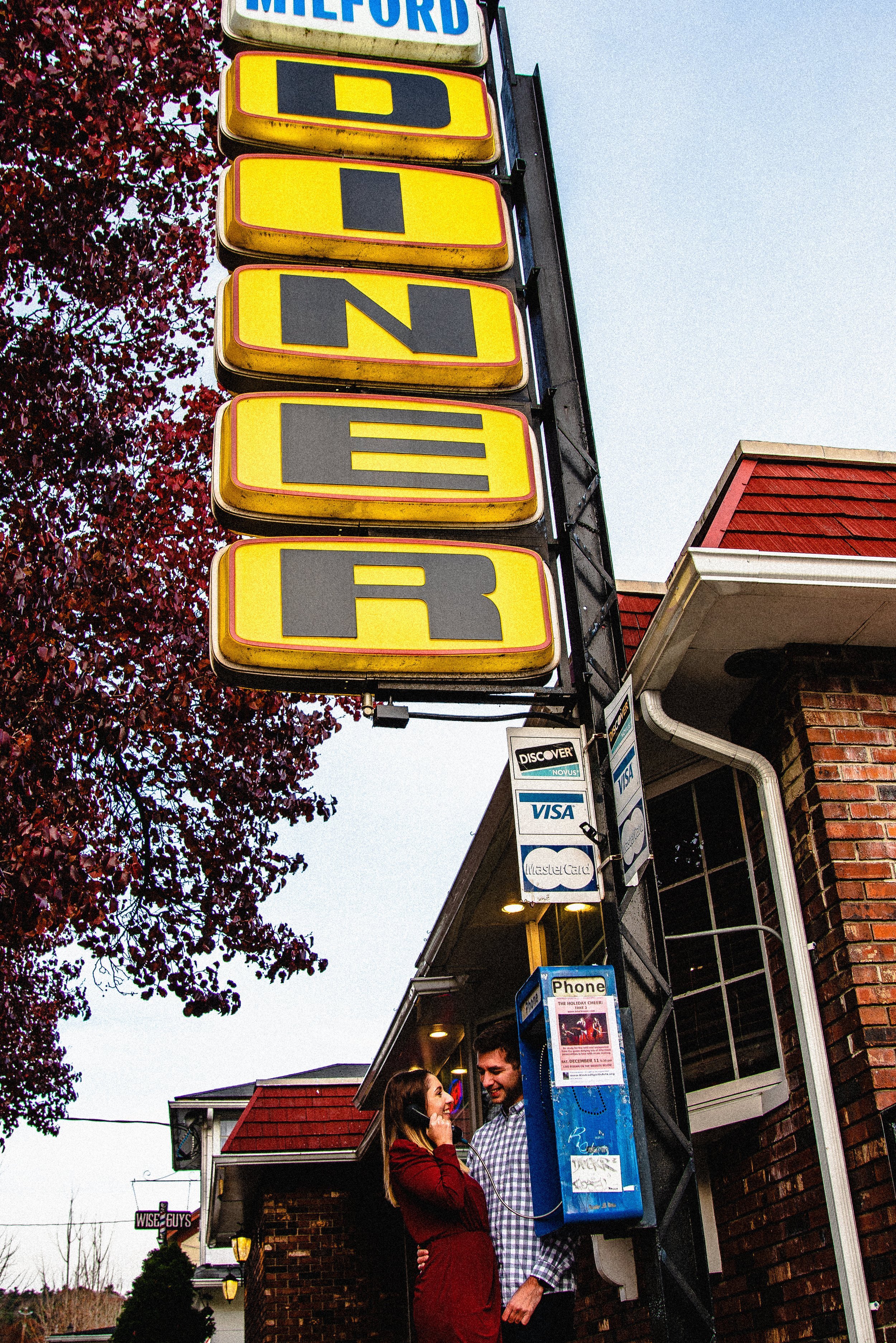 Couple talking outside a diner with a large diner sign and a blue payphone.