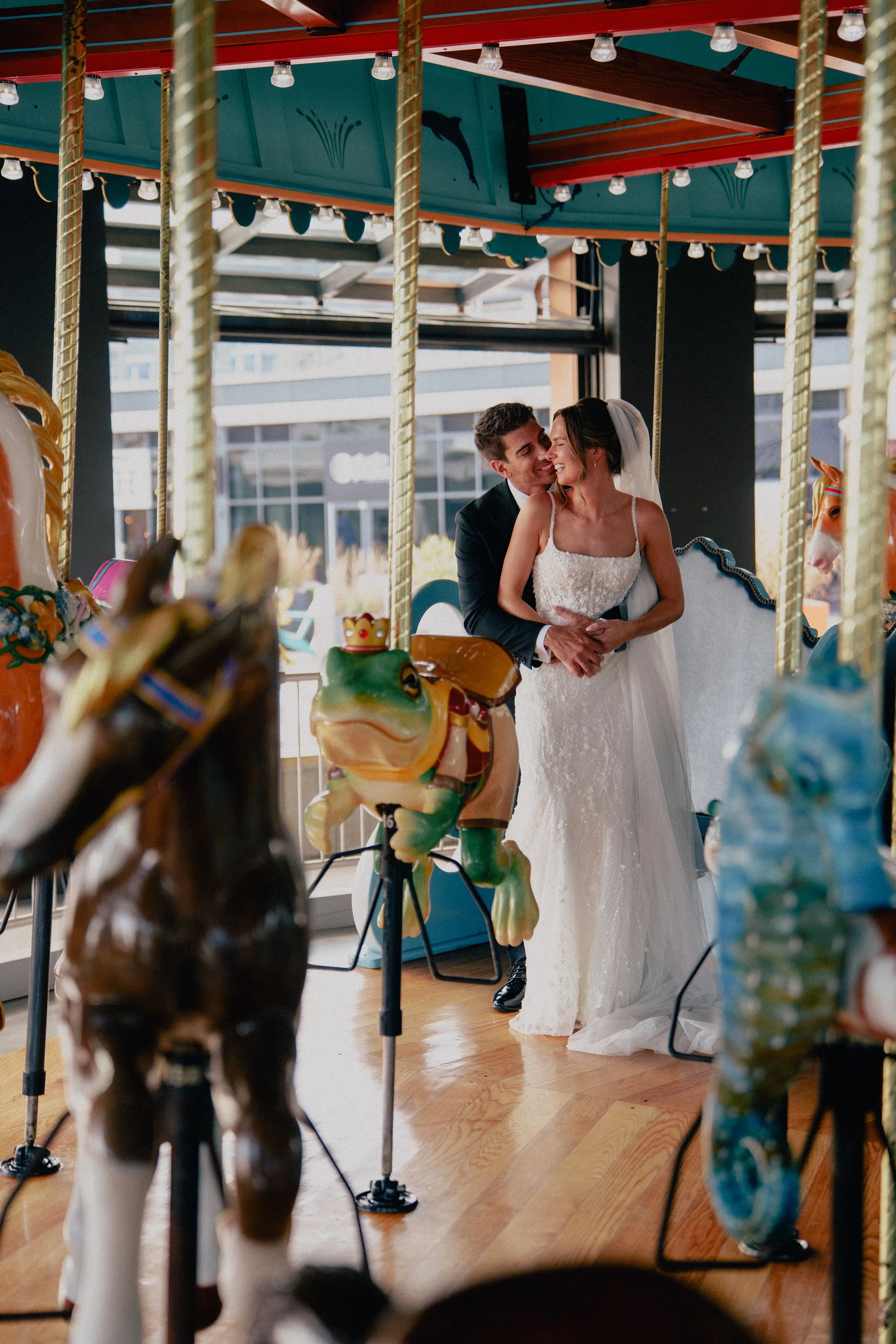 A happy nj wedding couple, a man in a tuxedo and a woman in a white wedding dress, sharing an intimate moment on a vintage carousel ride, surrounded by carousel horses and decor at wave resort - Wedding photographers- Timeline Visuals
