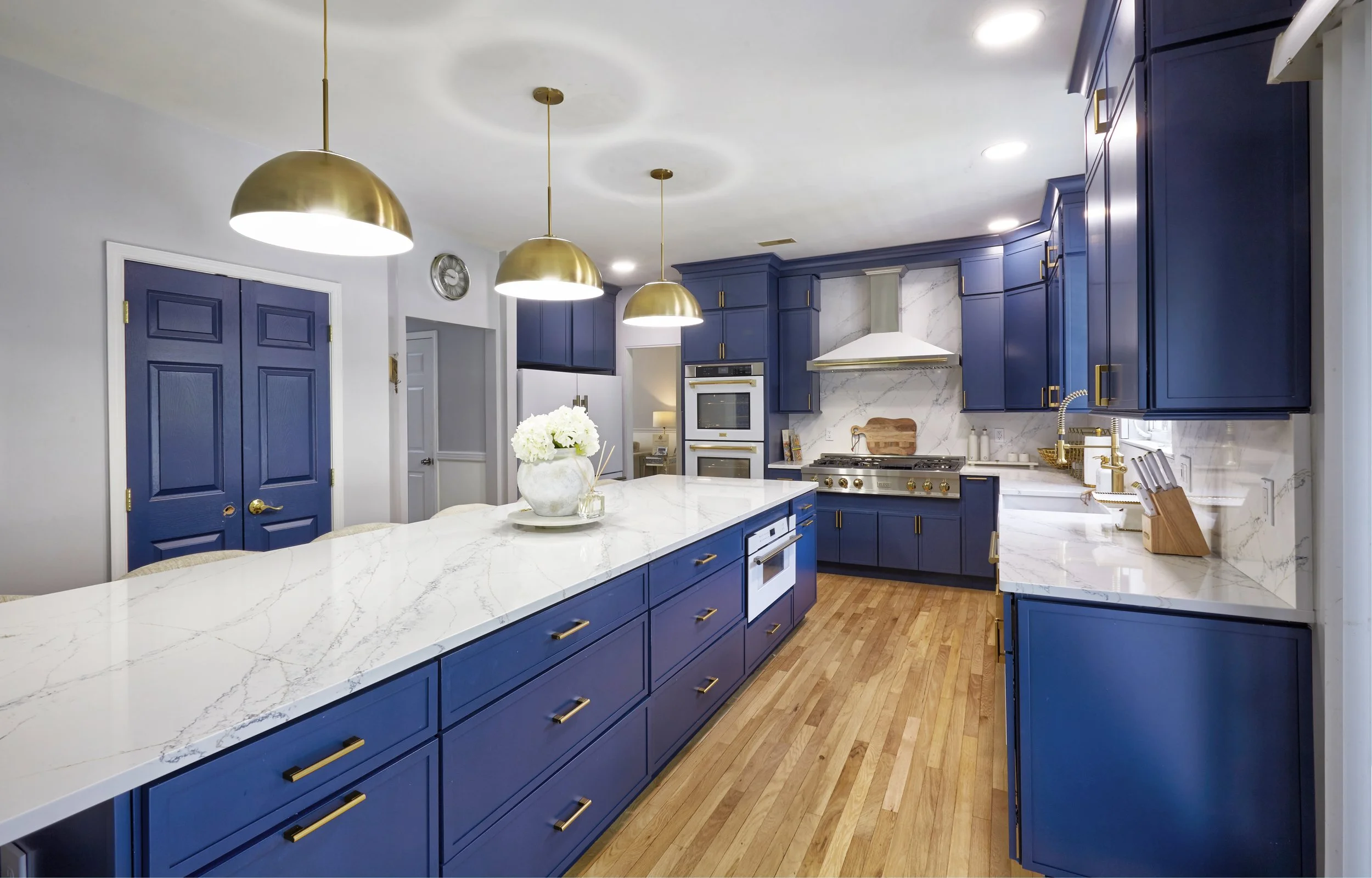 Modern kitchen with blue cabinets, white marble countertops, gold hardware, and hardwood floors.