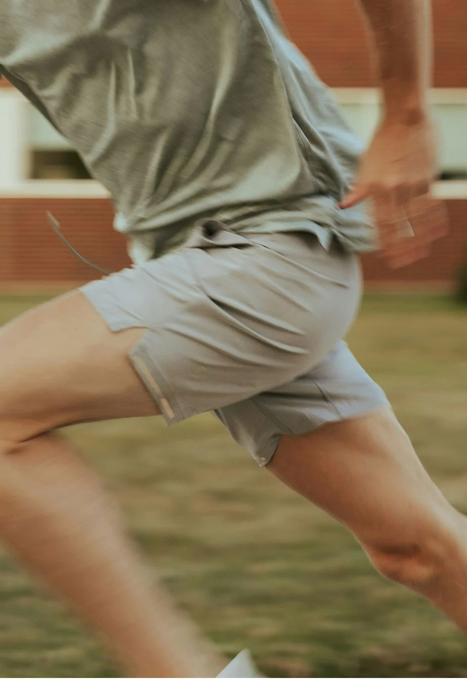 A person running outdoors on grass, wearing a gray shirt and gray shorts.