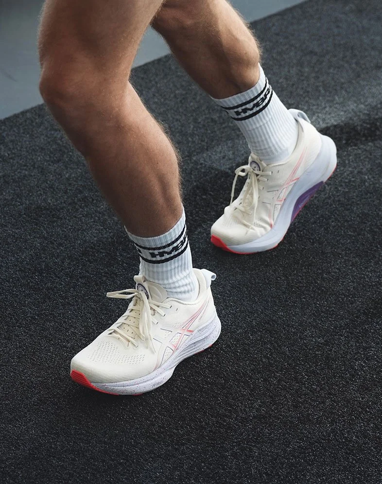 Close-up of a person's legs with muscular calves, wearing white athletic sneakers and white socks with black stripes, on a black textured gym floor.