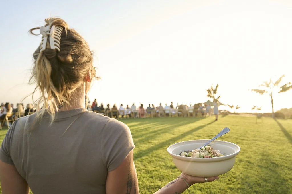 Guest carrying a seasonal salad at an outdoor long-table dinner