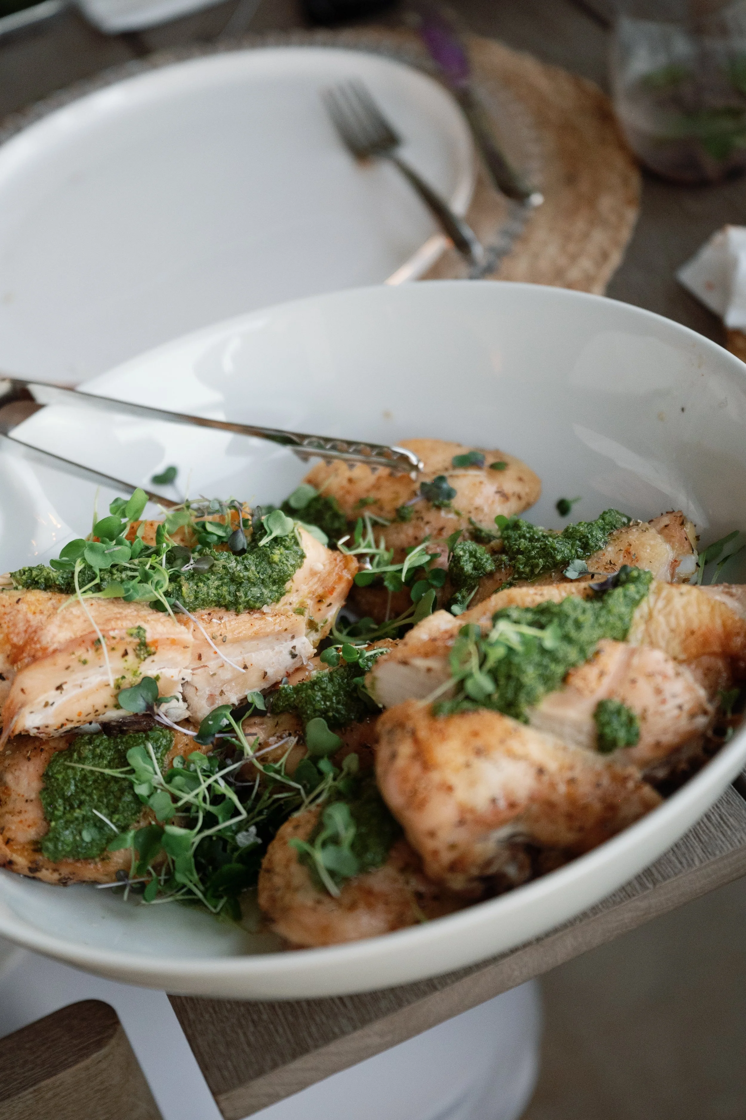 Cooked chicken breasts topped with green pesto sauce and microgreens in a white oval dish.